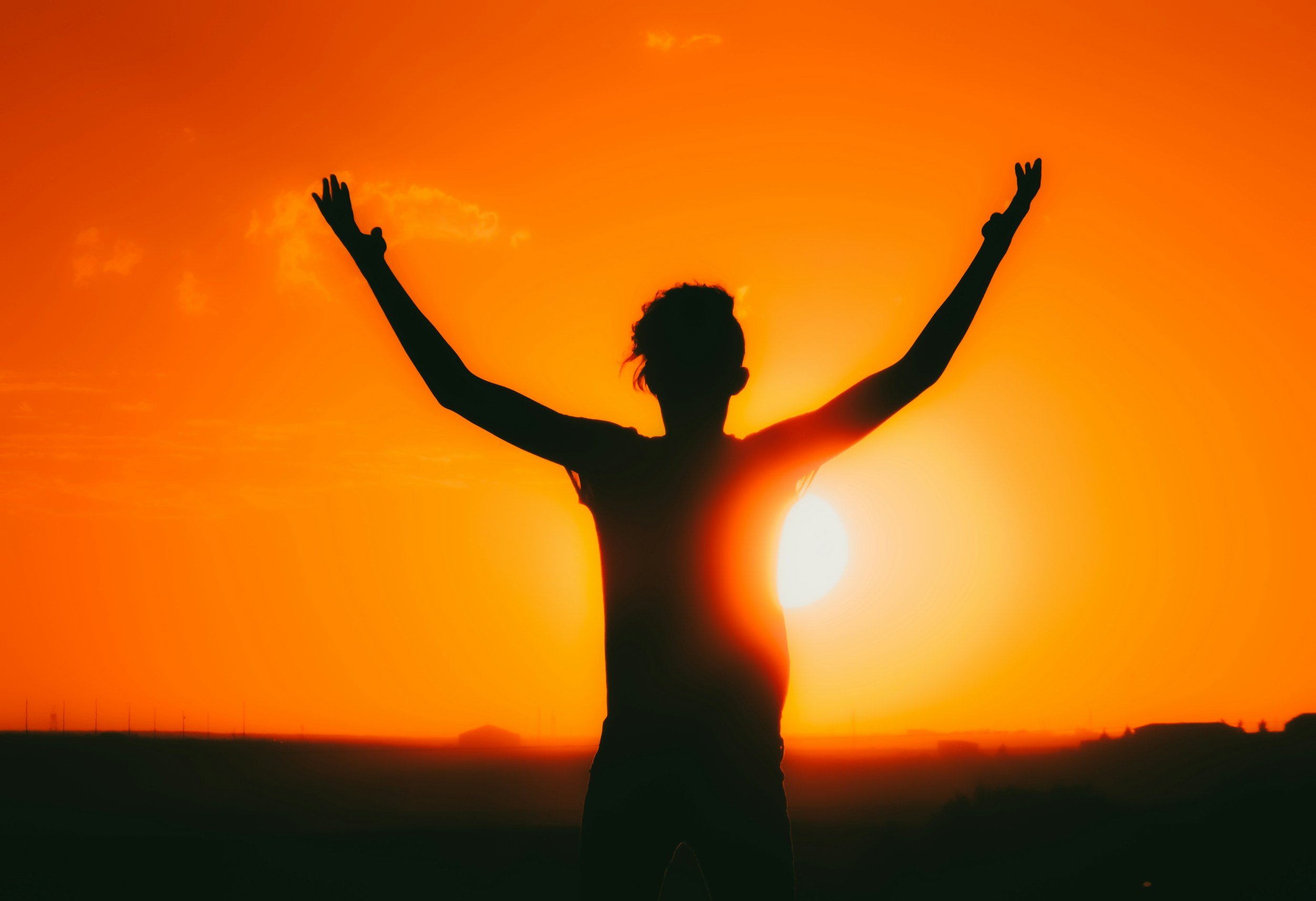 Person with arms raised celebrating during sunset in a rural landscape.