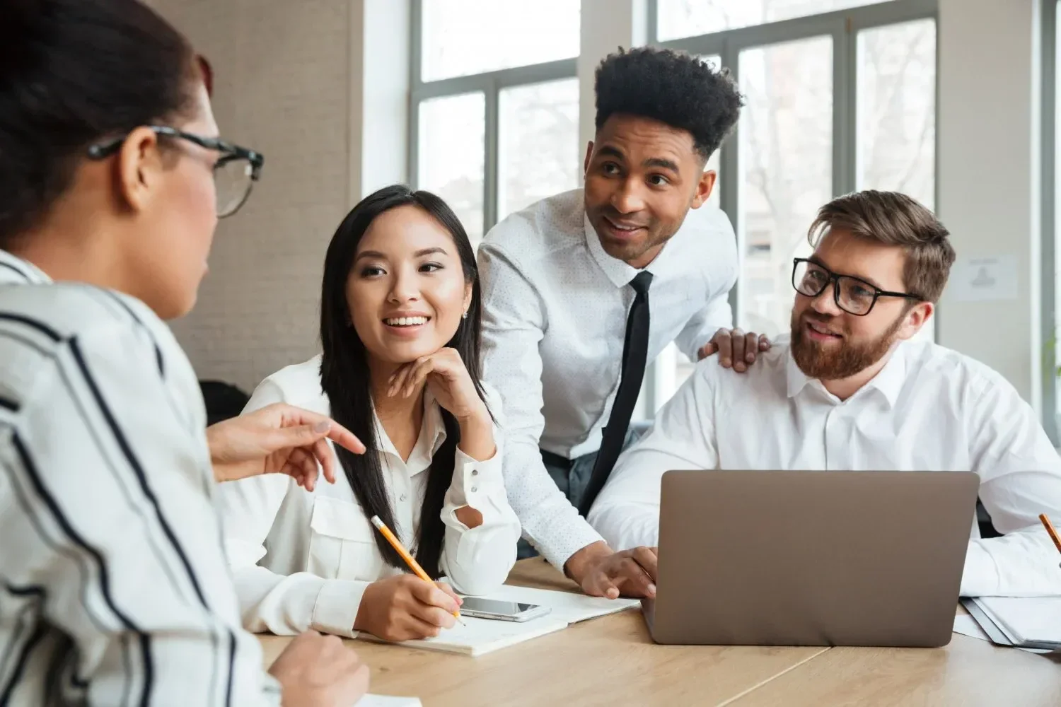 A diverse group of four colleagues in smart casual attire engage in a lively discussion around a conference table, conveying teamwork and collaboration.