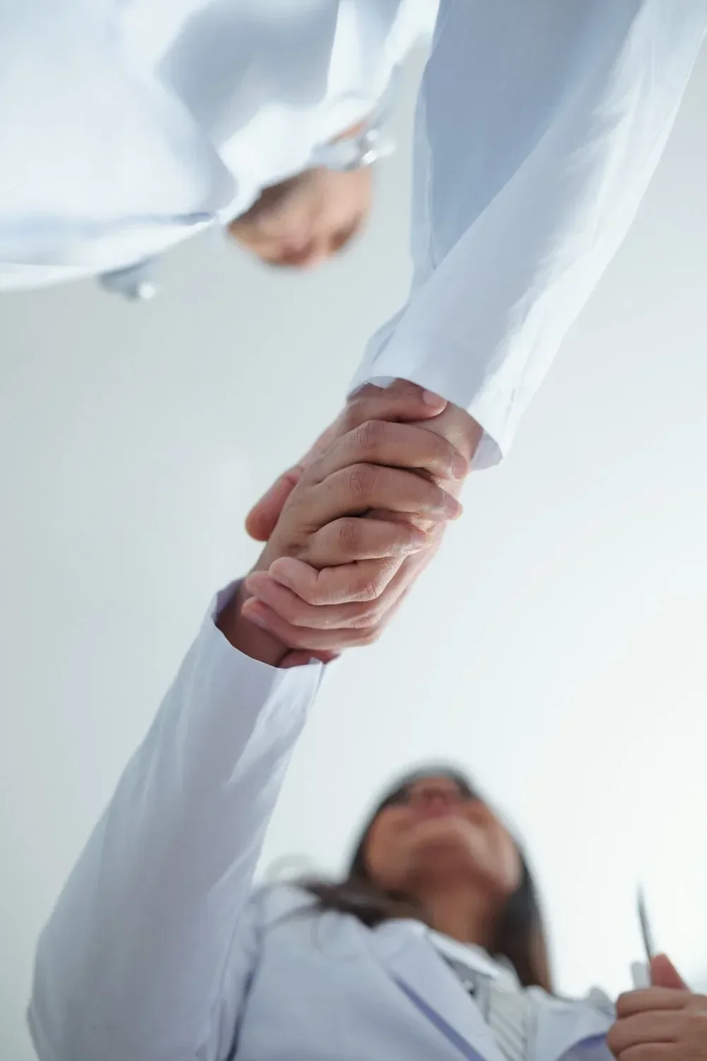 Two individuals in white coats shaking hands, viewed from below.