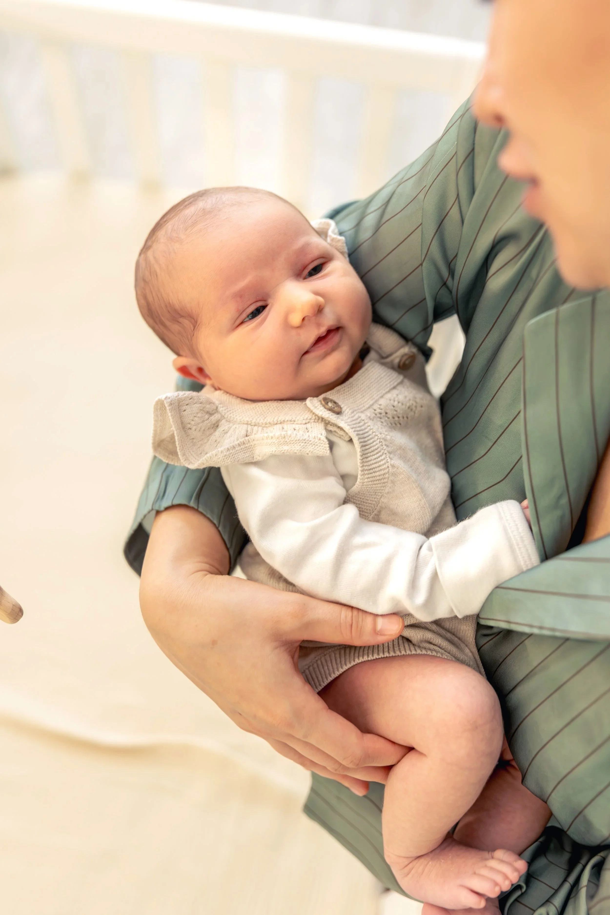 A person holding a baby close, with only part of their face visible, in a softly lit indoor setting.