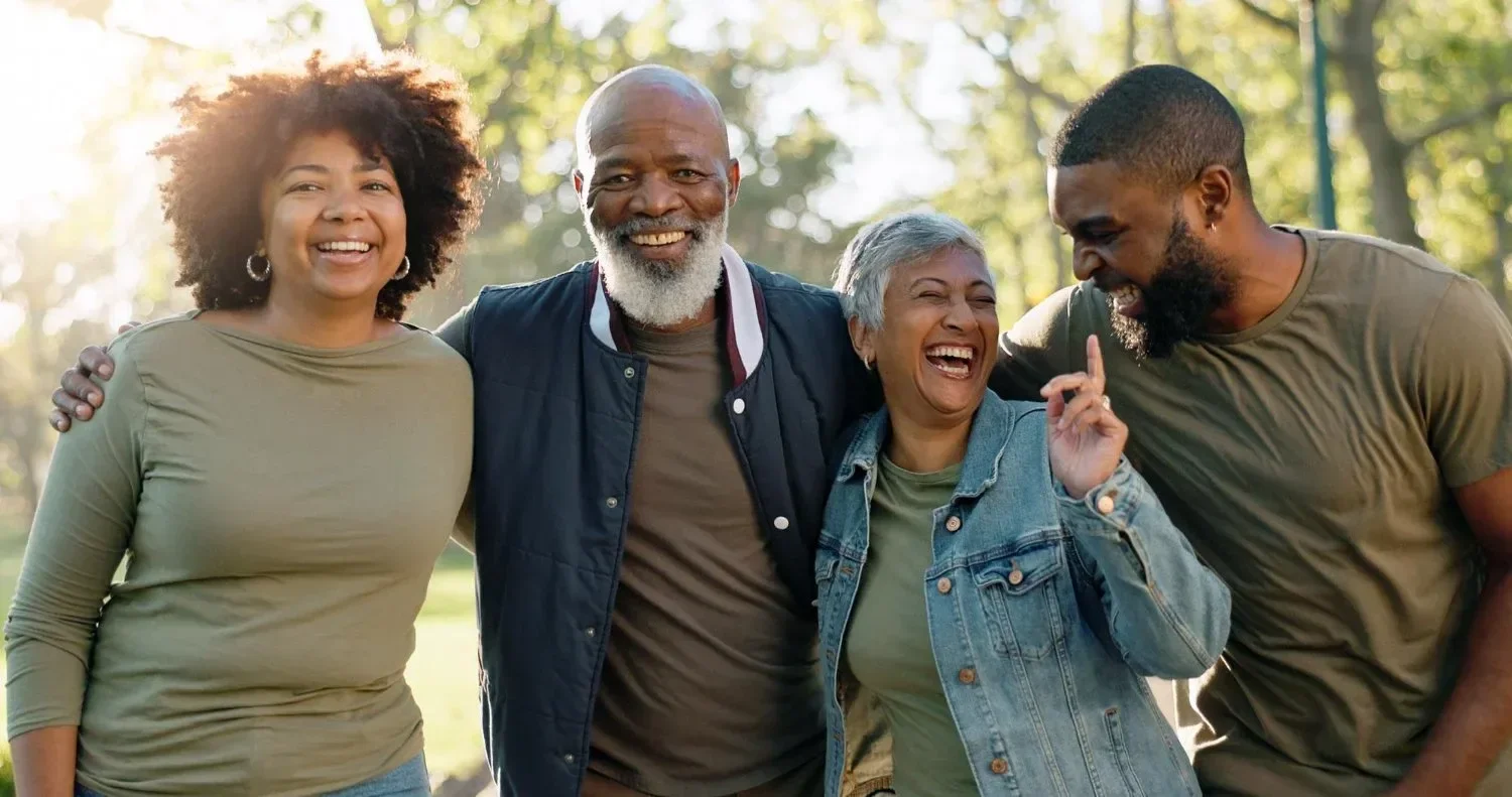 A family of four people stand close outdoors, smiling and laughing.