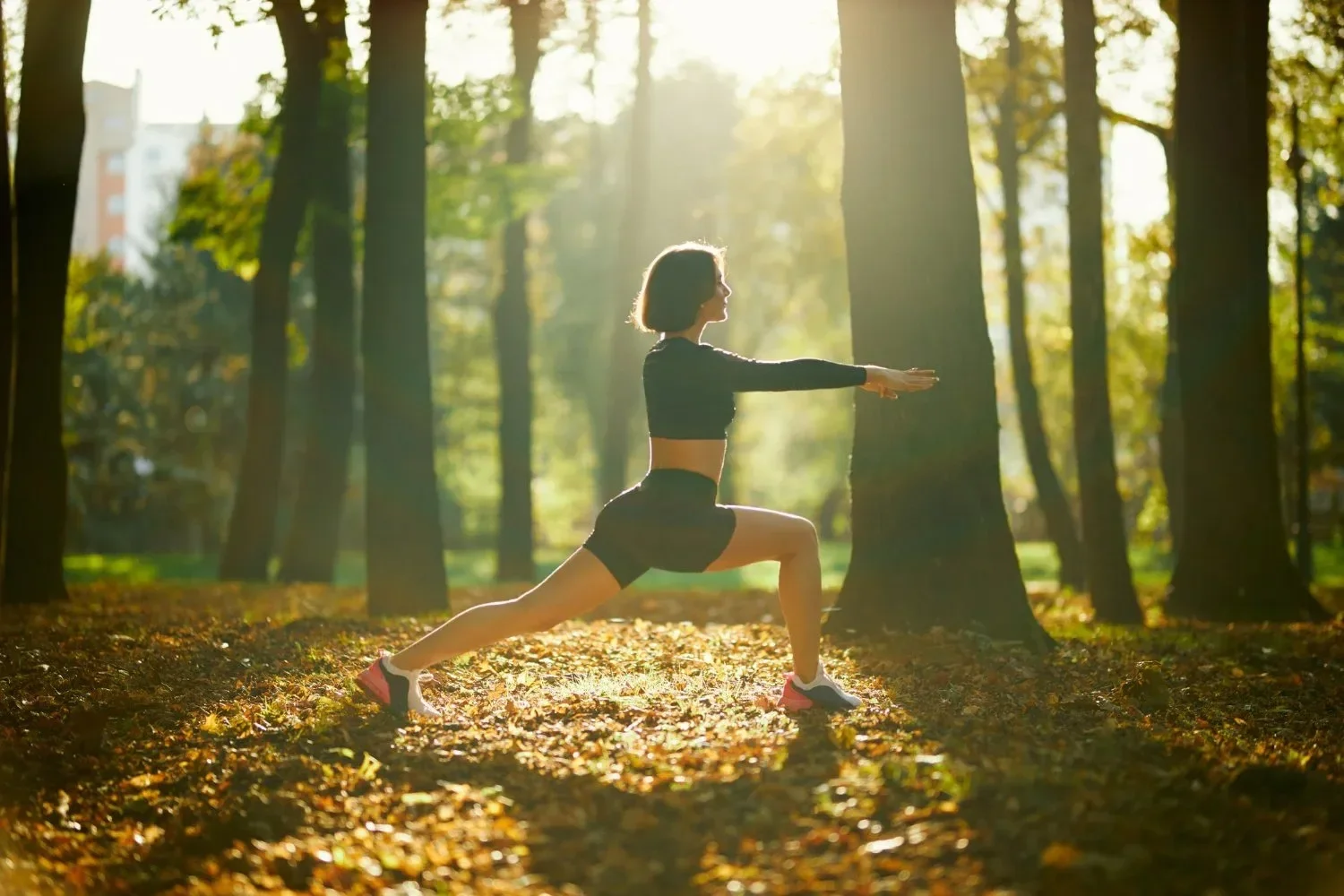 A woman exercises in a sunlit forest, performing a lunge.