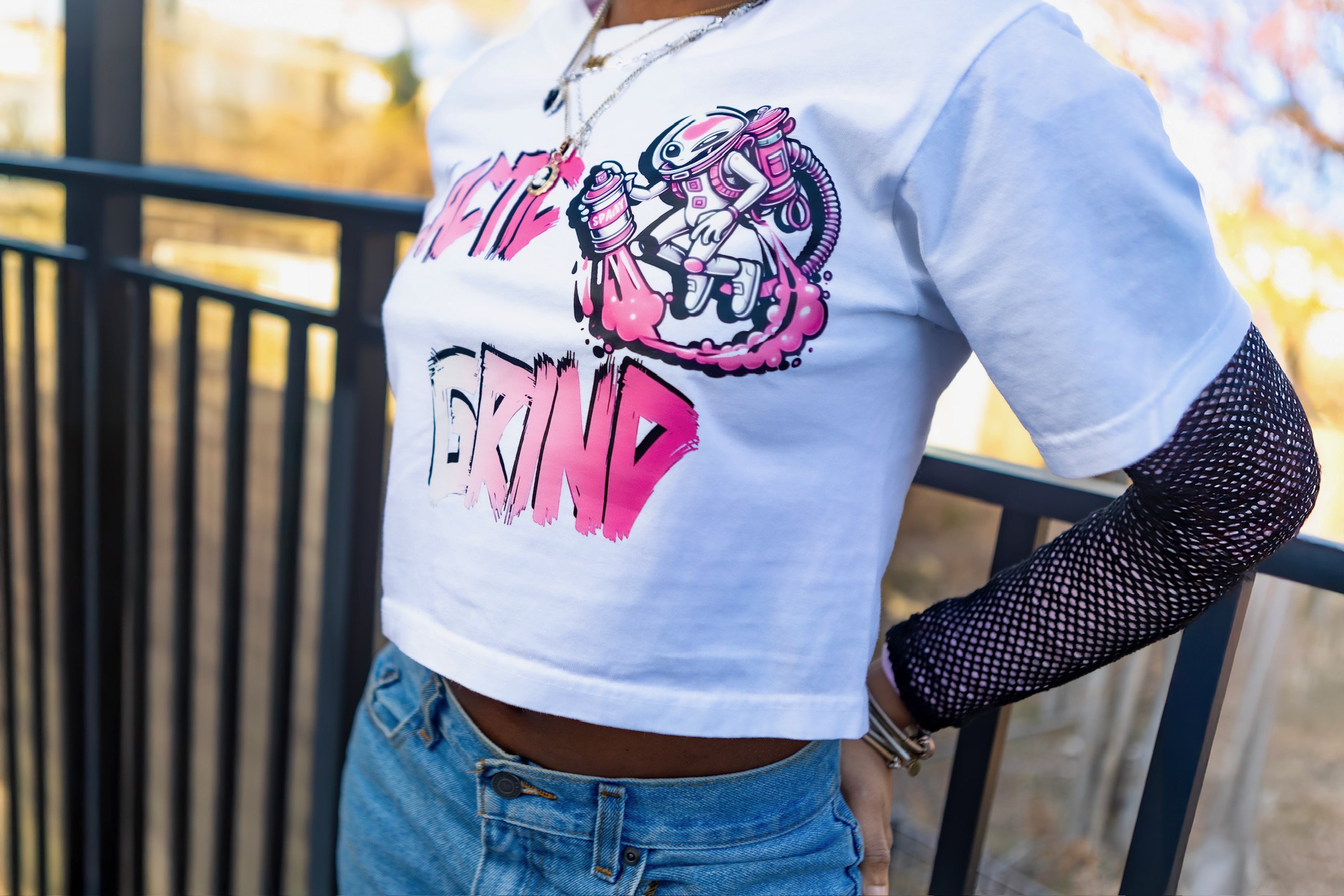 Person wearing a white t-shirt with a colorful graphic of an astronaut riding a rocket and spray paint, with the words 'My Dream' in pink, layered over a black mesh long-sleeve shirt, and blue jeans.