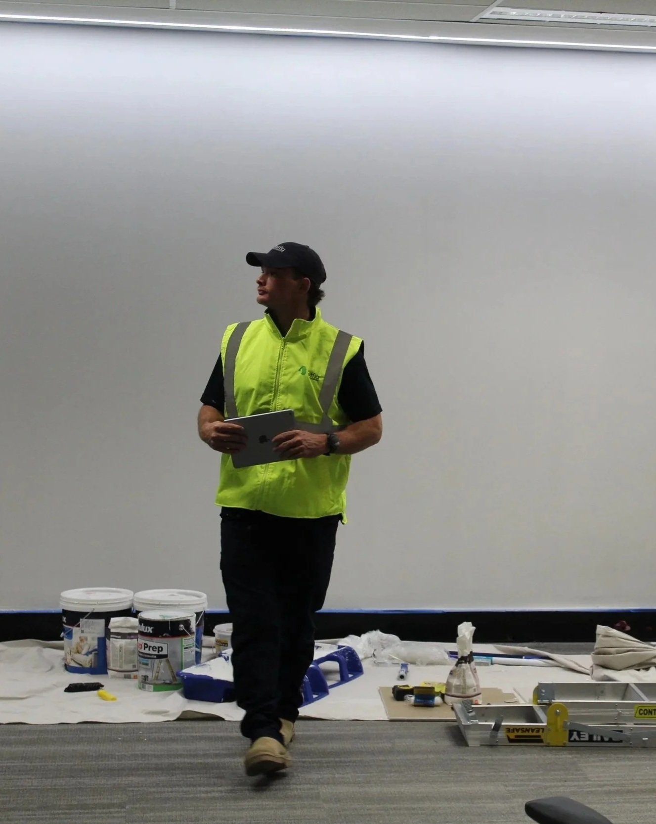 A man in a yellow safety vest holding an iPad, standing in front of construction supplies and tools on a white tarp.