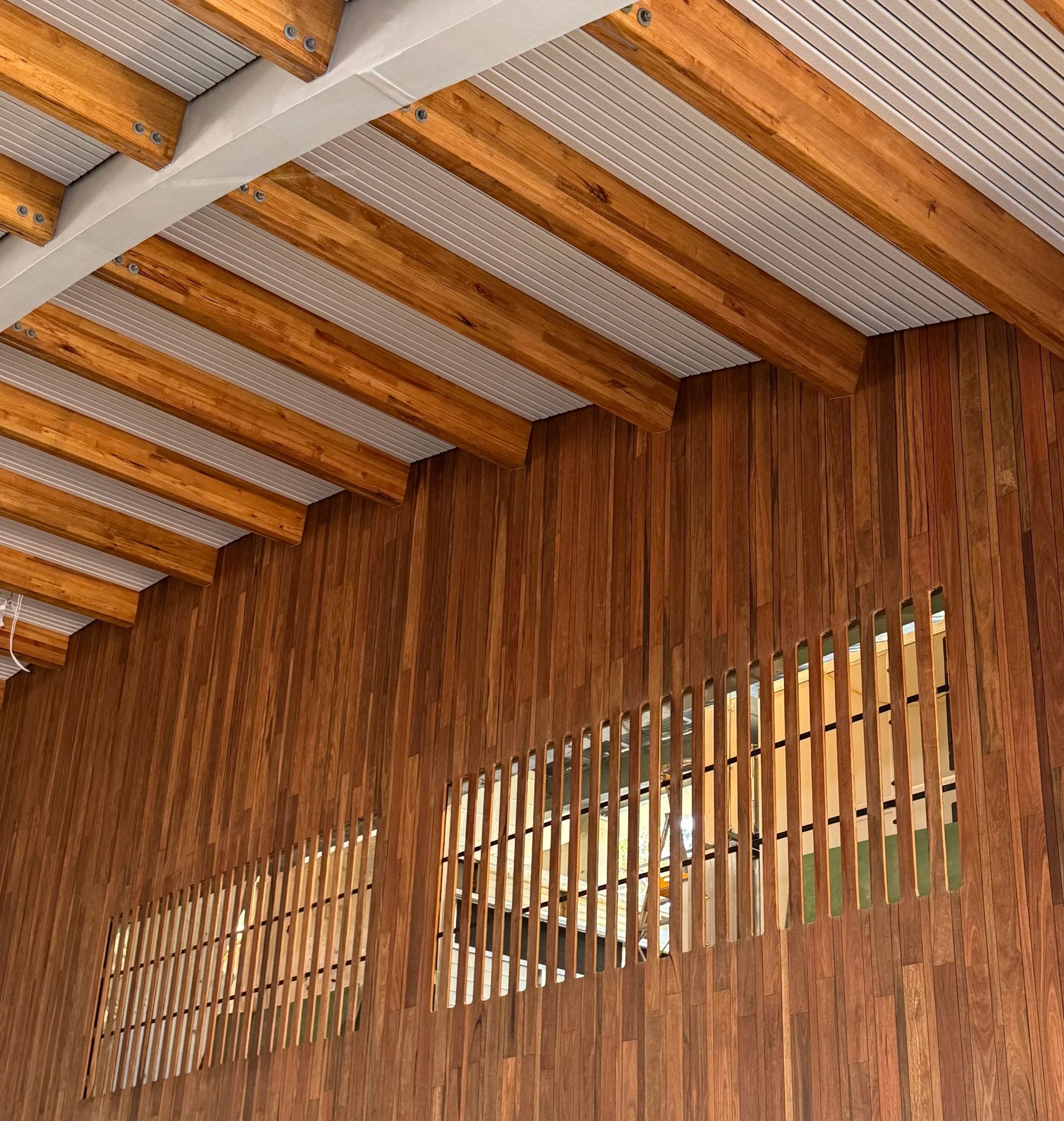 Interior with wooden slat walls and ceiling beams, with a cut-out window in the wall showing an outdoor space.