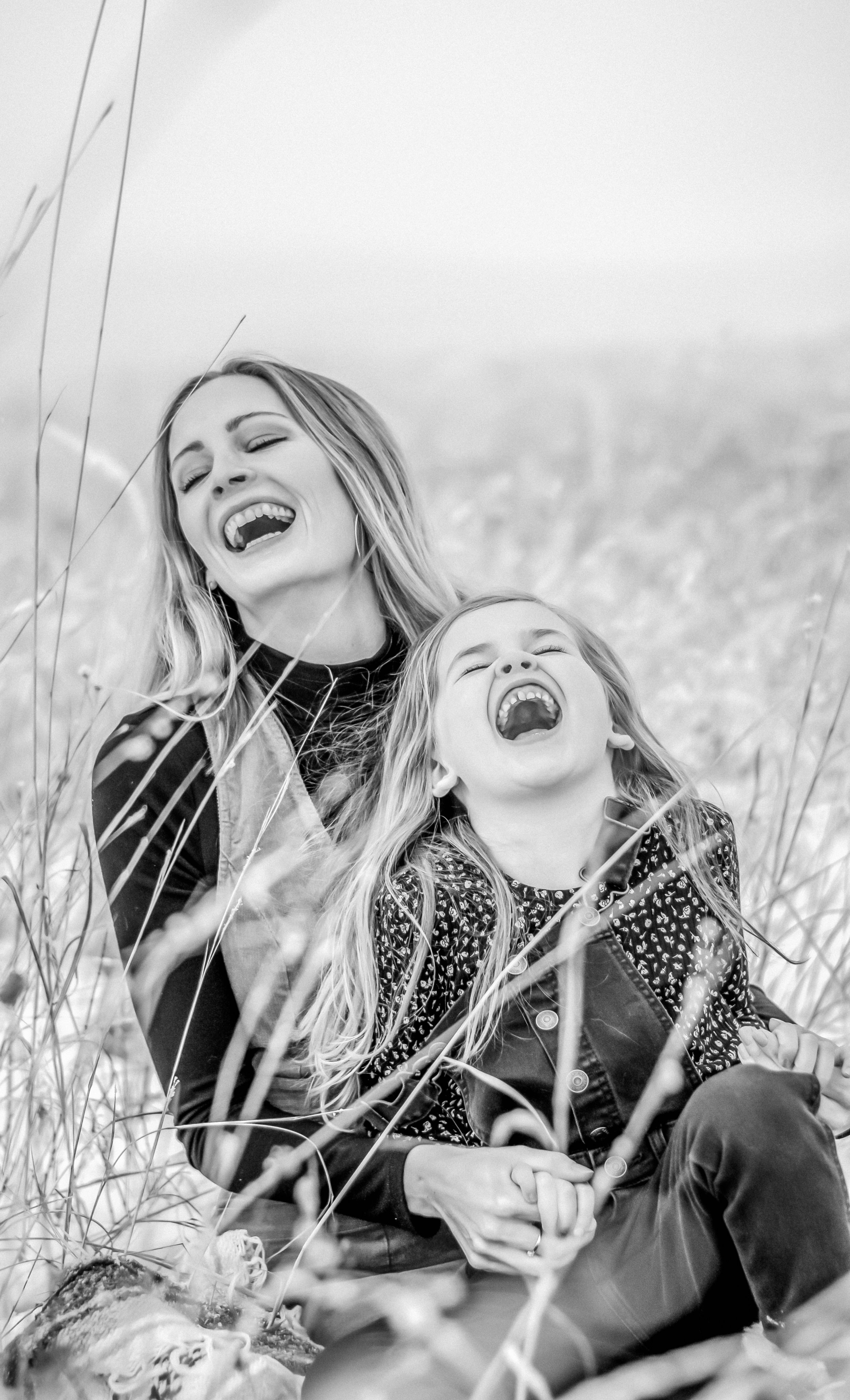 A woman and a young girl are laughing and enjoying themselves outdoors in a field of tall grass.