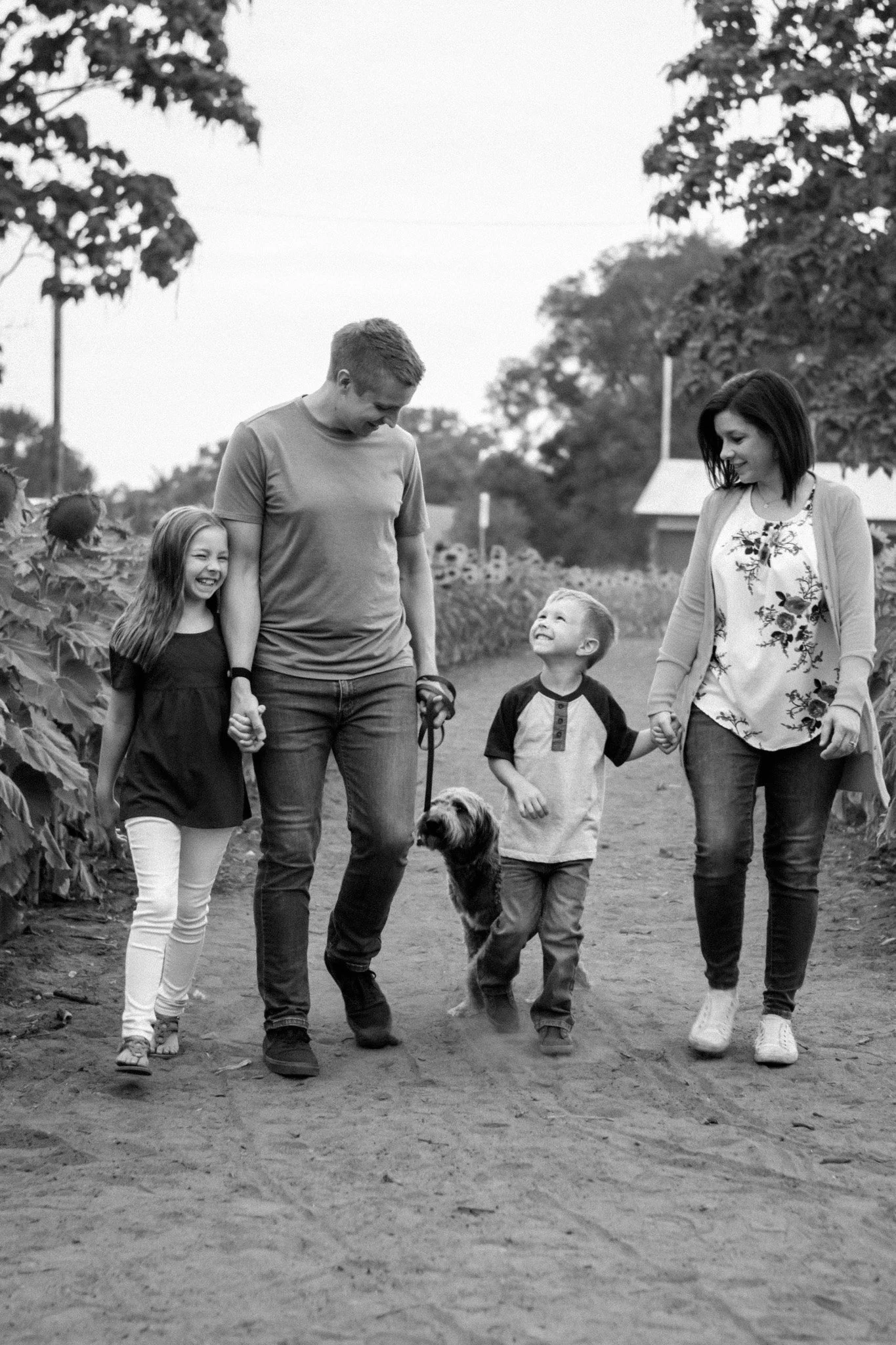 Family walking with dog in a field, holding hands, smiling, in black and white.