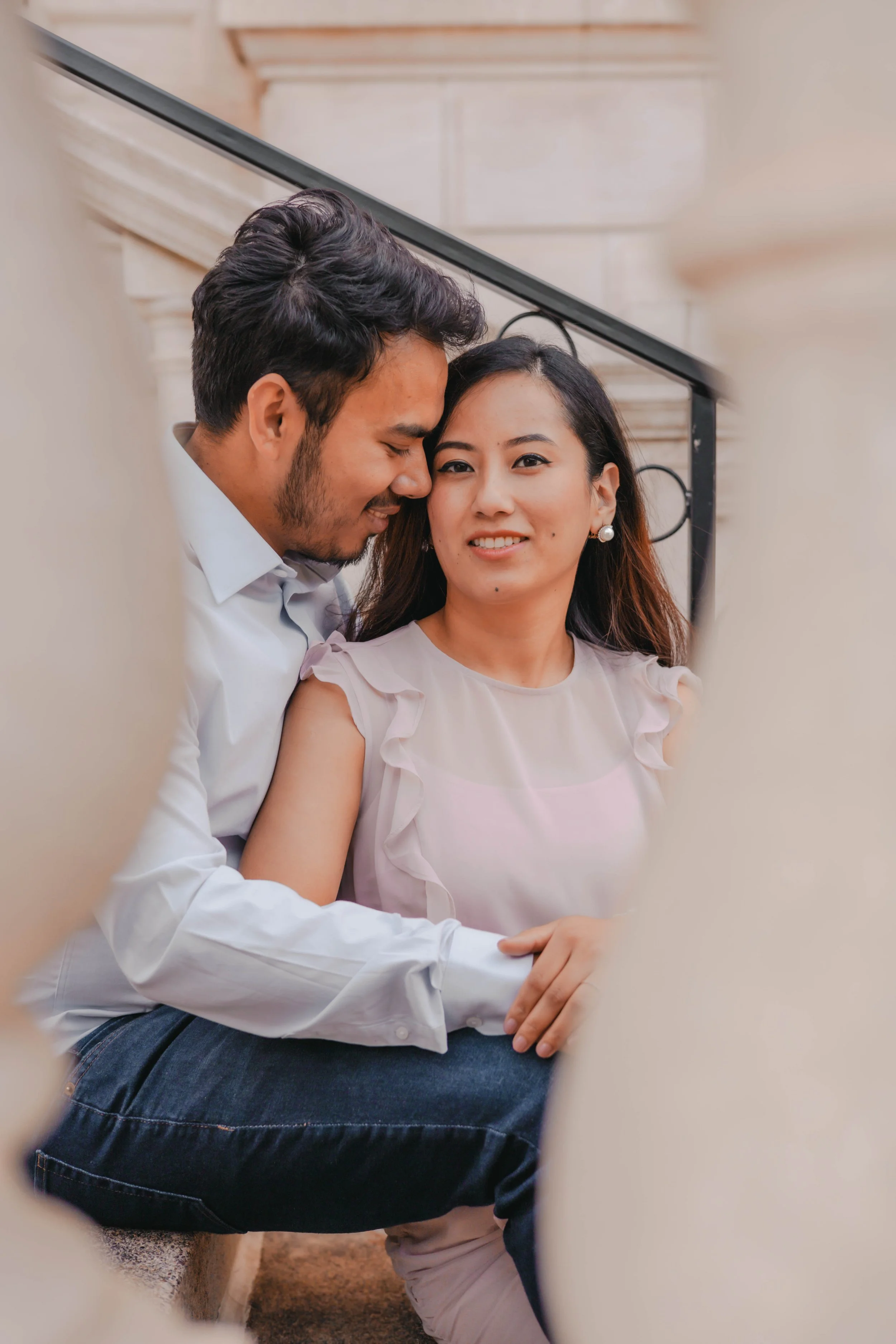 A couple sitting on a staircase, with the man whispering into the woman's ear and the woman smiling