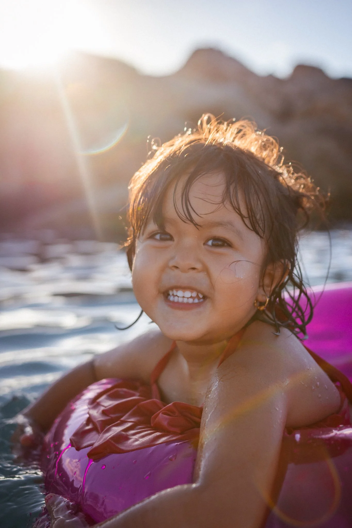 Young girl smiling while floating in water with a pink inner tube during sunset