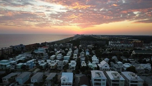 Coastal neighborhood with houses and a sunset over the ocean.