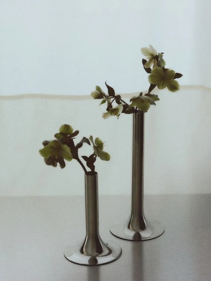 Two metal vases with small green and white flowers on a white surface against a light background.