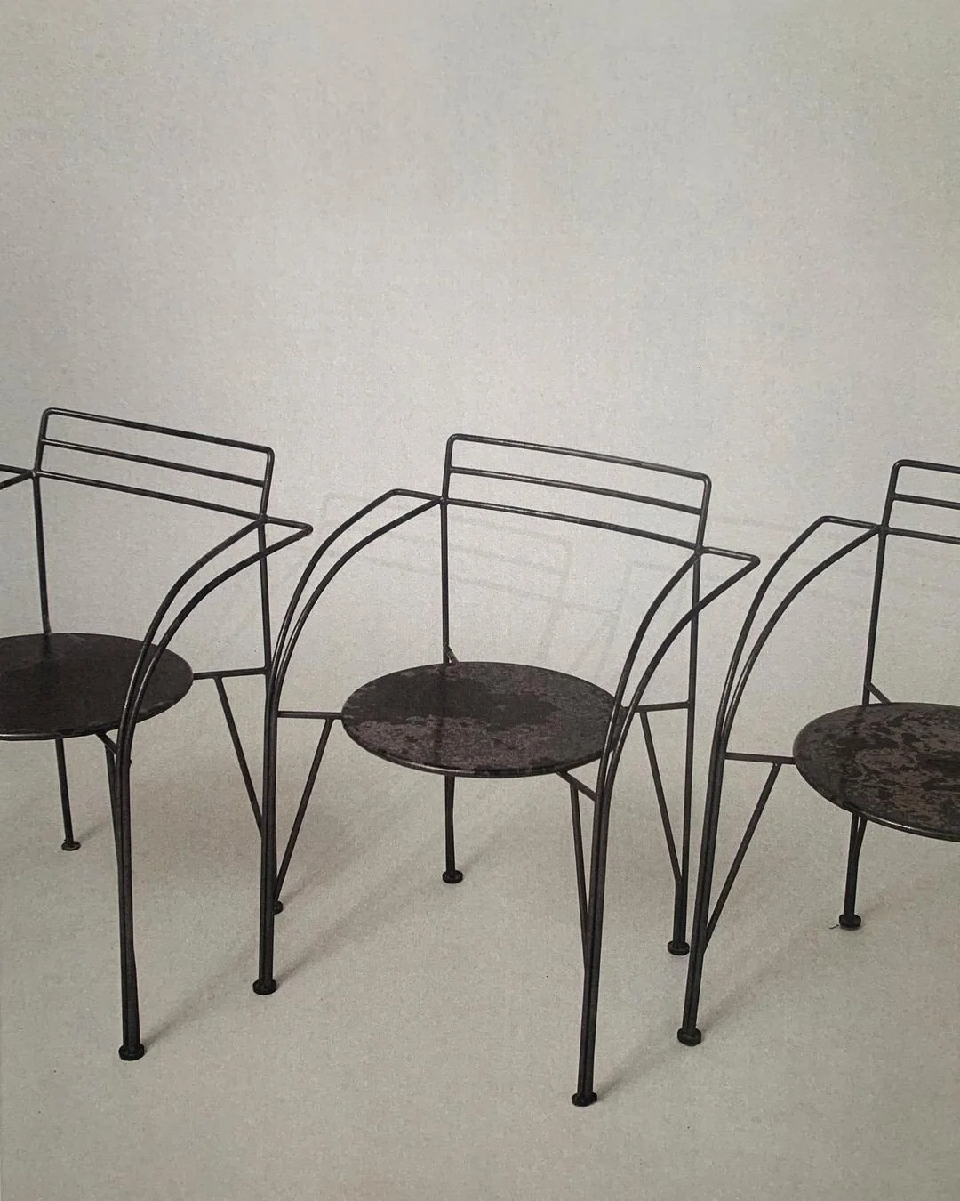 Three black metal chairs with round seats in a plain room with a light-colored wall
