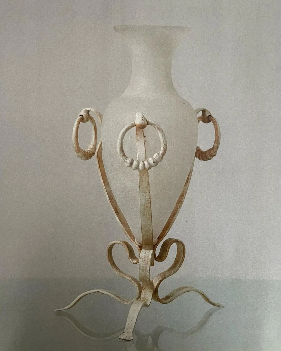 Vintage white ceramic vase with ornate metal stand featuring decorative scroll and ring details.