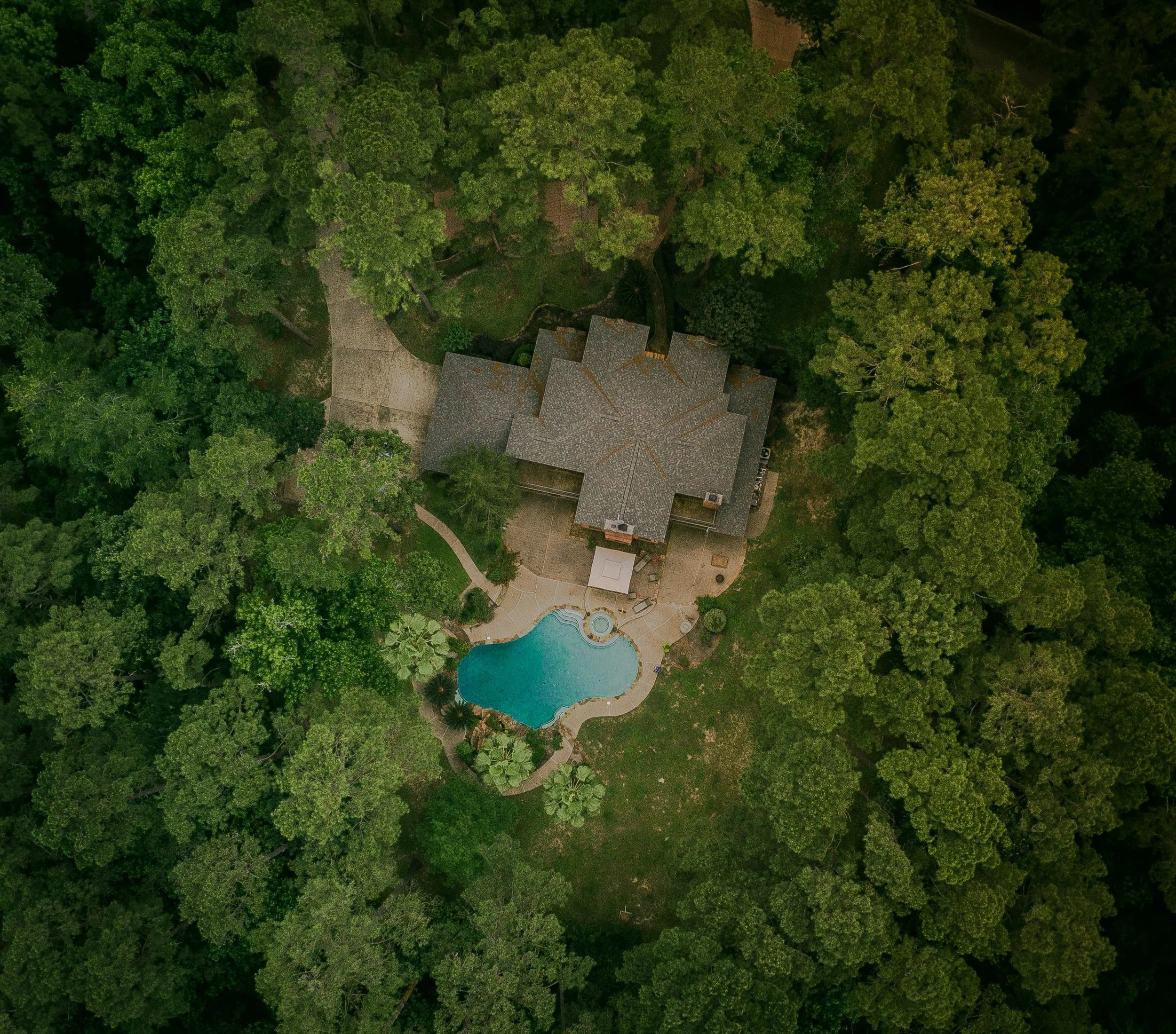 Aerial view of a house with a swimming pool surrounded by dense green trees.
