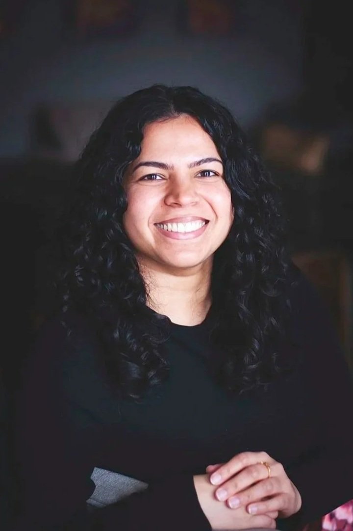 portrait de Rishana Nooman, femme brune avec veste foncée, assise sun canapé