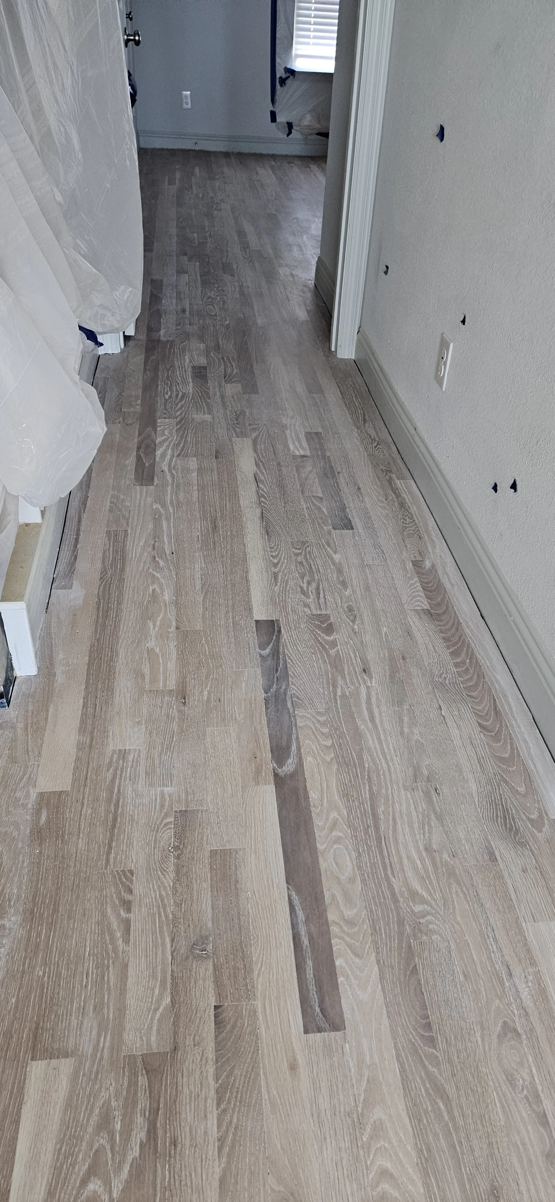 Newly installed wooden flooring in a hallway leading to a room with a window and curtain.
