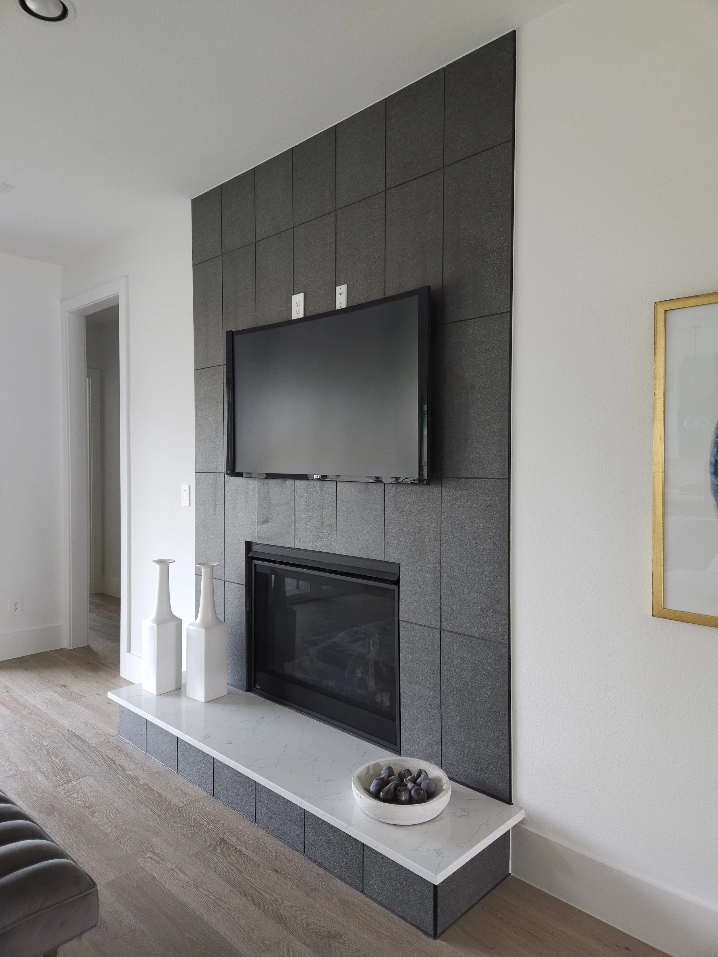 Living room fireplace with a mounted flat-screen TV above and decorative vases and a bowl of stones on the white marble hearth.