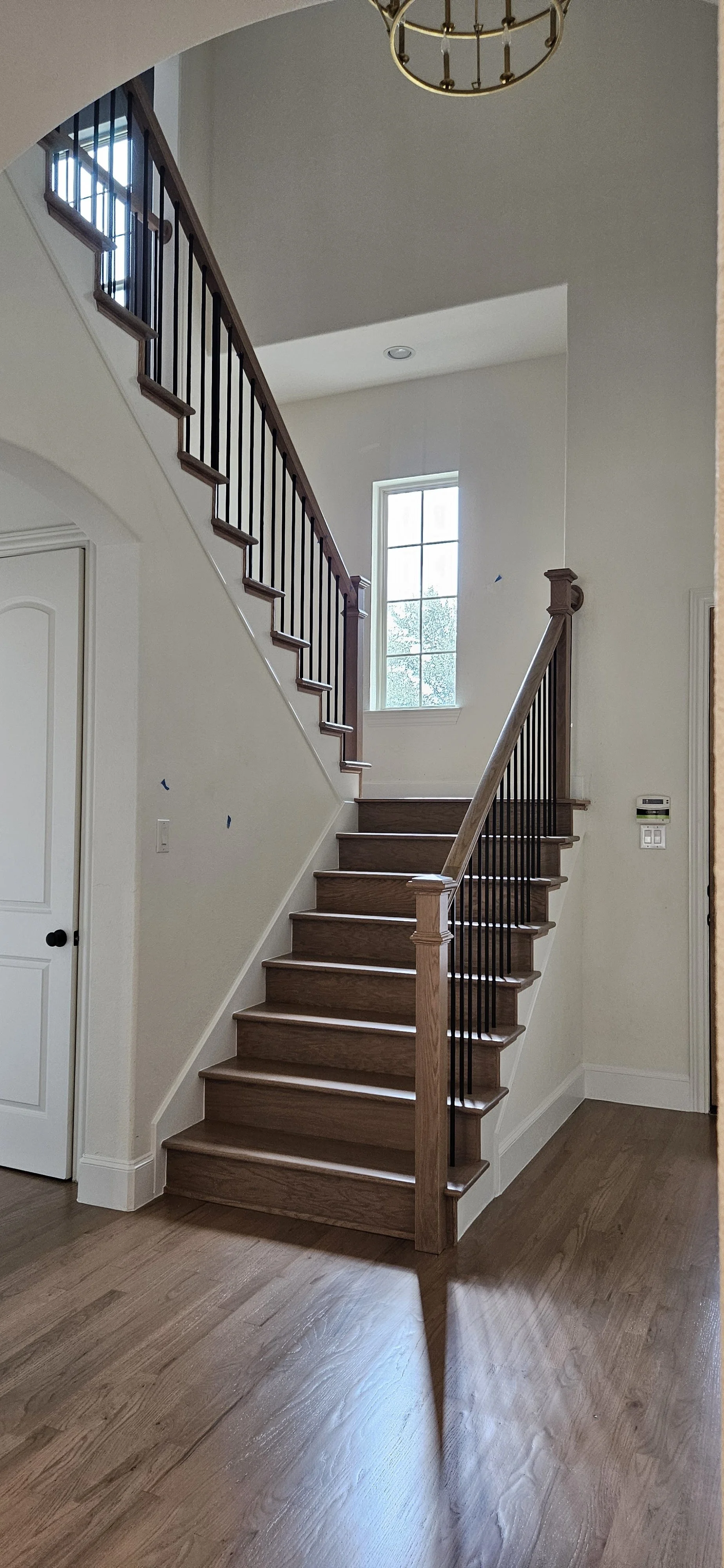 Empty staircase with wooden steps and a wooden handrail leading to a second floor, Next to a window letting in natural light, in a residential interior.