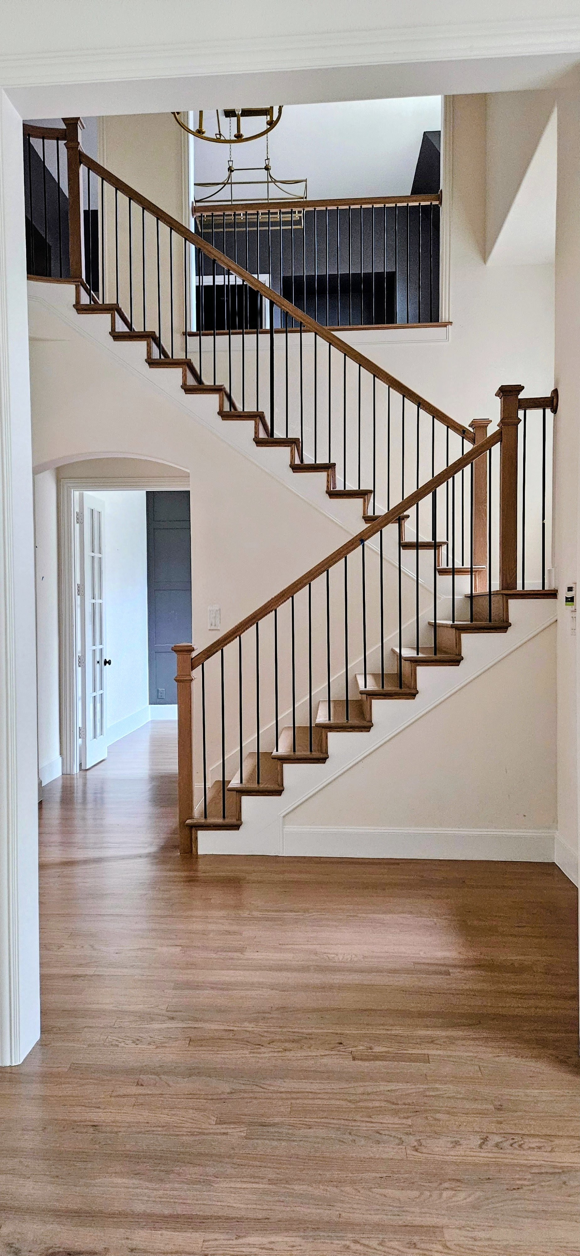 Interior view of a staircase with wooden steps and black metal railing, leading to an upper floor in a home.