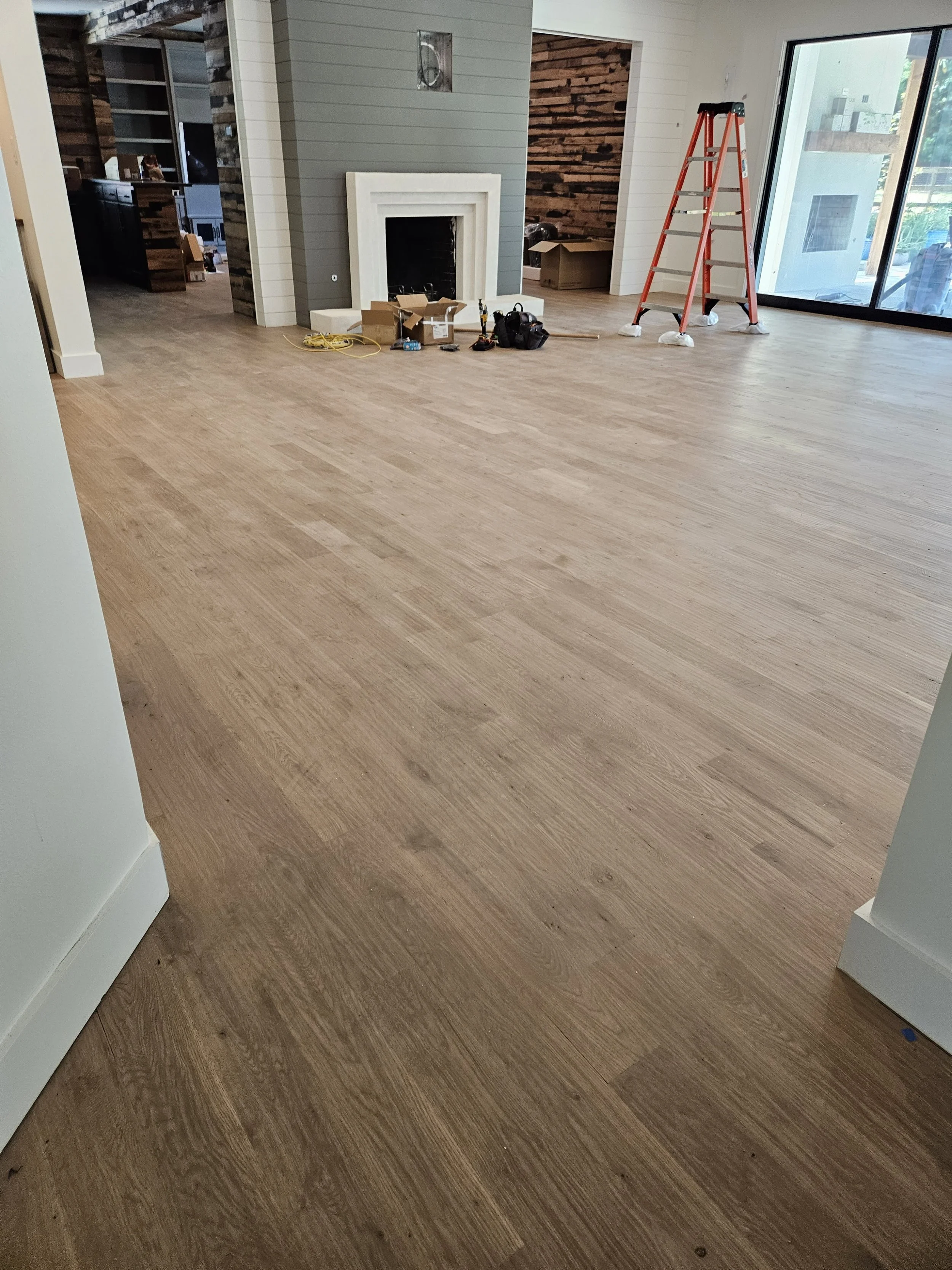 Living room with wooden flooring, construction tools, a step ladder, and an unfinished fireplace.