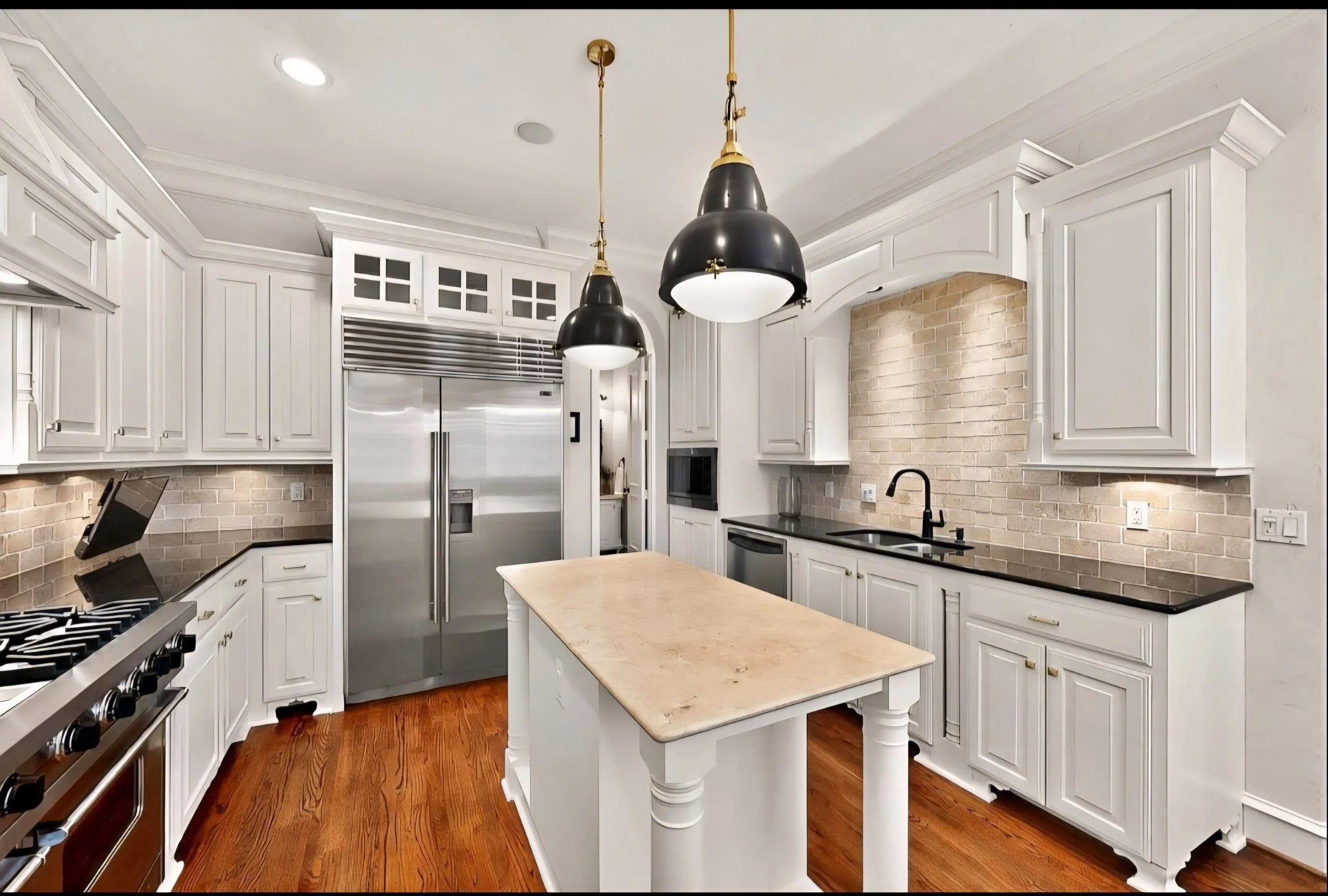 Modern kitchen with white cabinets, black countertops, a central island with a beige marble top, stainless steel refrigerator, microwave, stove, and black pendant lights, hardwood flooring, and a brick accent wall behind the sink.