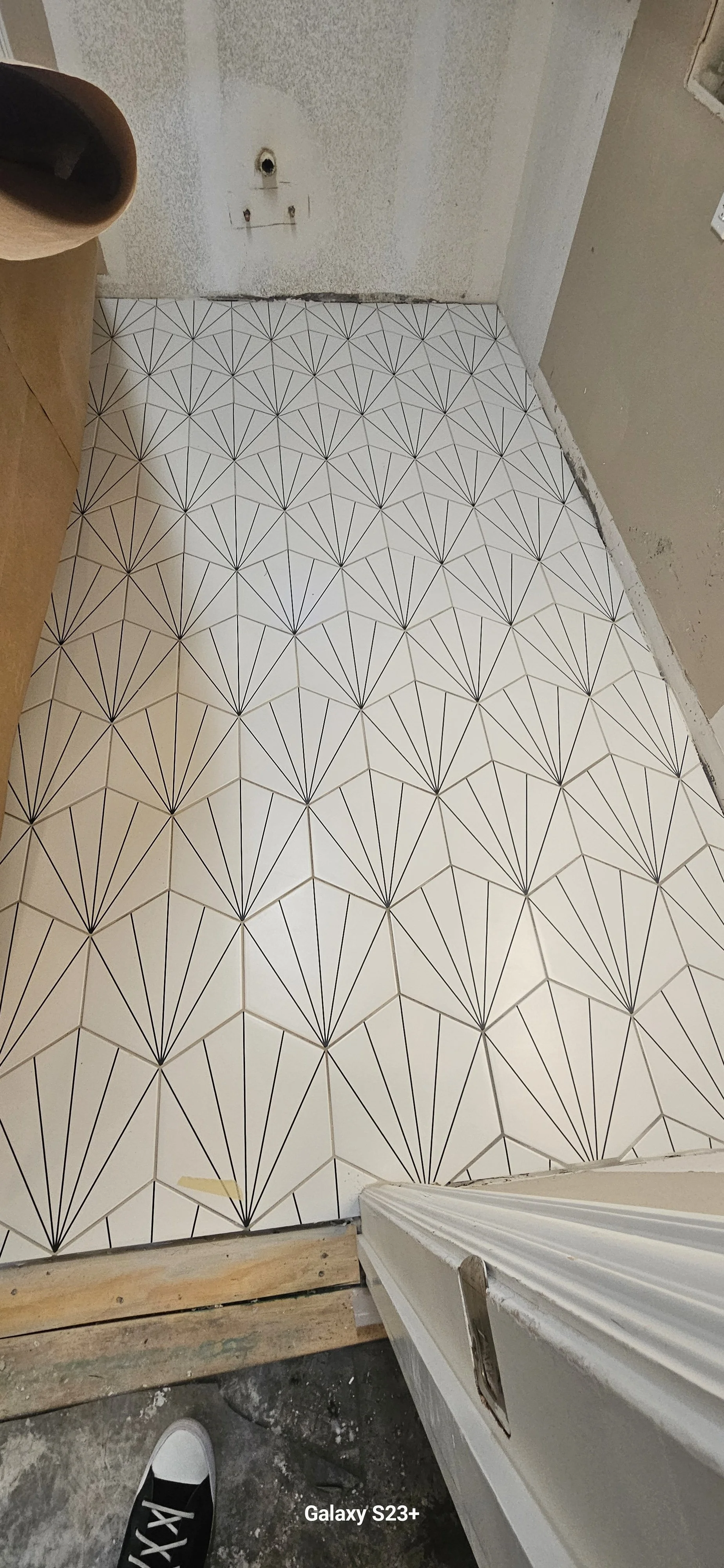 Tiled floor with geometric black and white pattern in a room under renovation, with a hole in the wall and construction materials visible.
