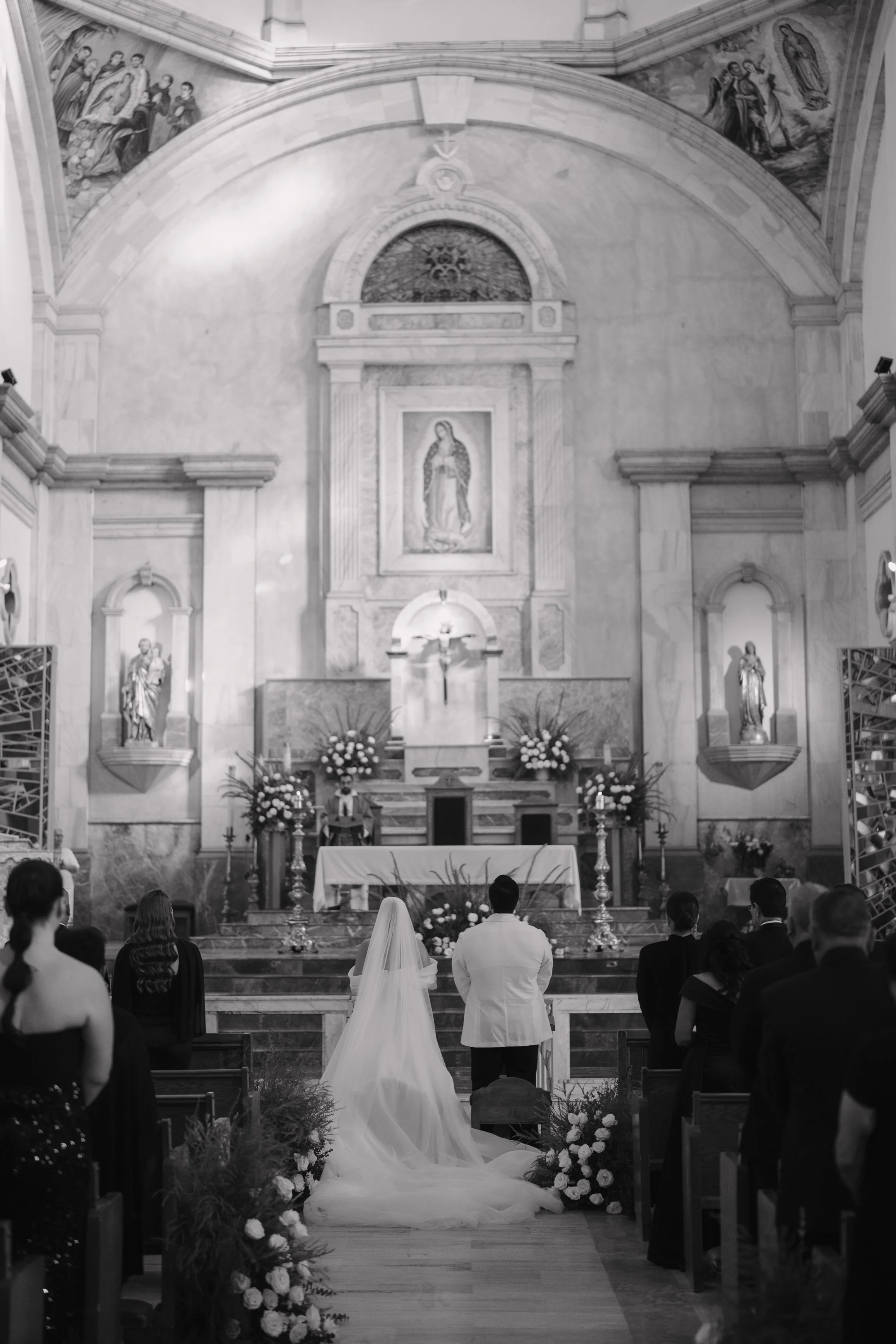 A wedding ceremony taking place inside a church with the bride and groom standing at the altar, surrounded by seated guests. Wedding Photography in Valle de Guadalupe, Ensenada, Baja California.