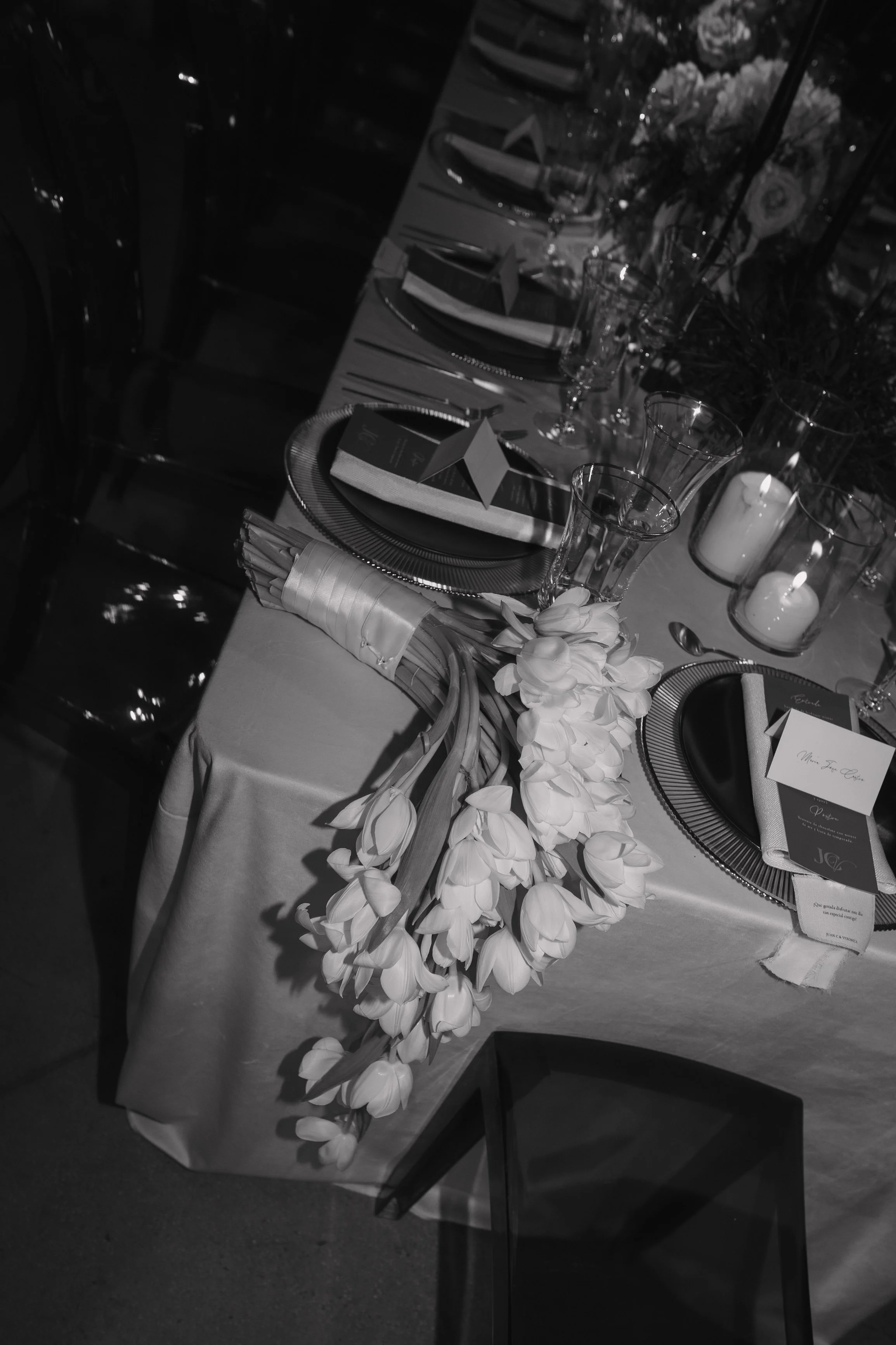 An elegantly set dining table with floral centerpiece, candles, wine glasses, folded napkins, and place cards, prepared for a special event or celebration. Wedding Photography in Valle de Guadalupe, Ensenada, Baja California.