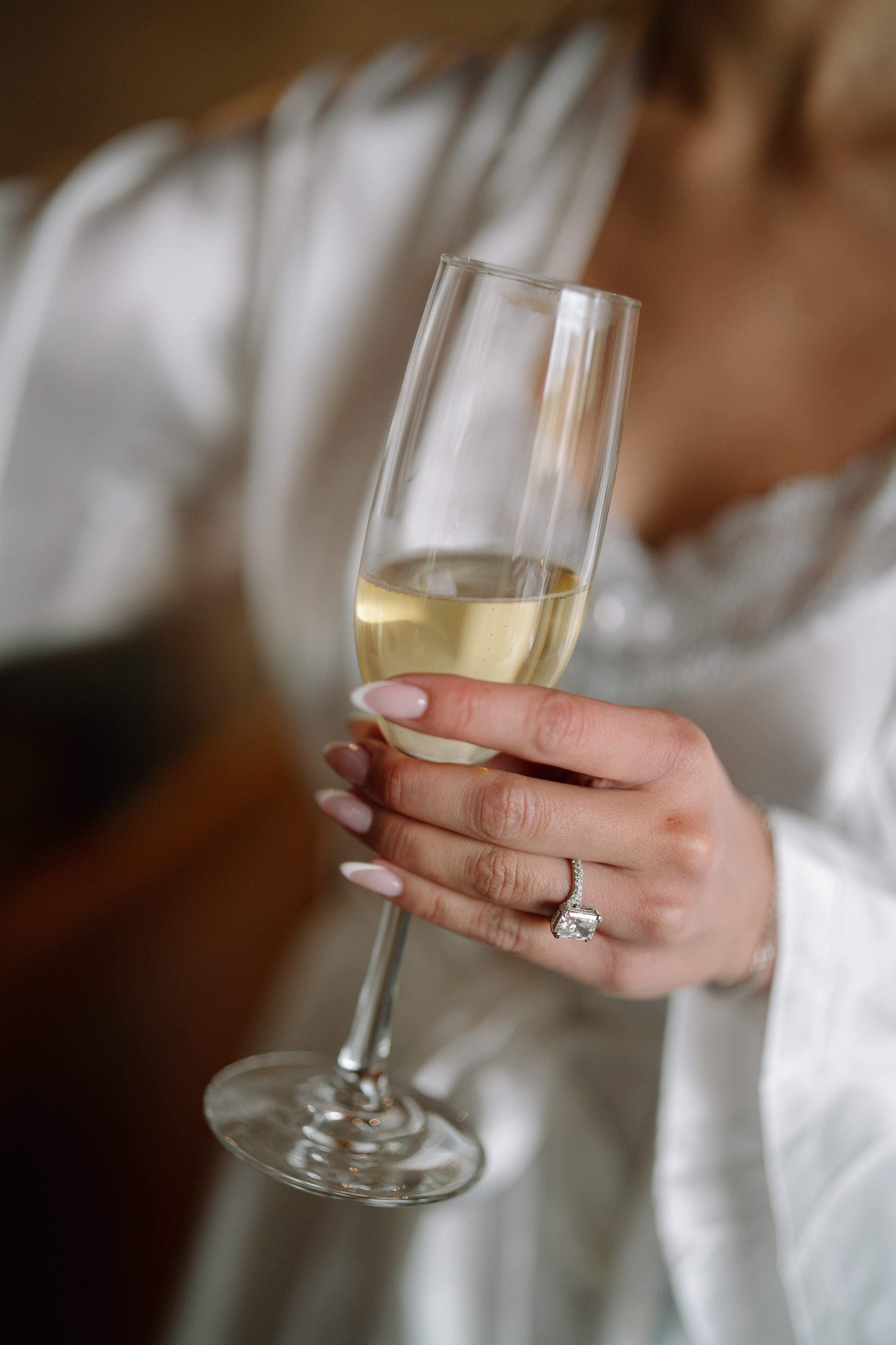 A woman holding a glass of white wine, showing a large wedding ring on her finger. Wedding Photography in Valle de Guadalupe, Ensenada, Baja California.
