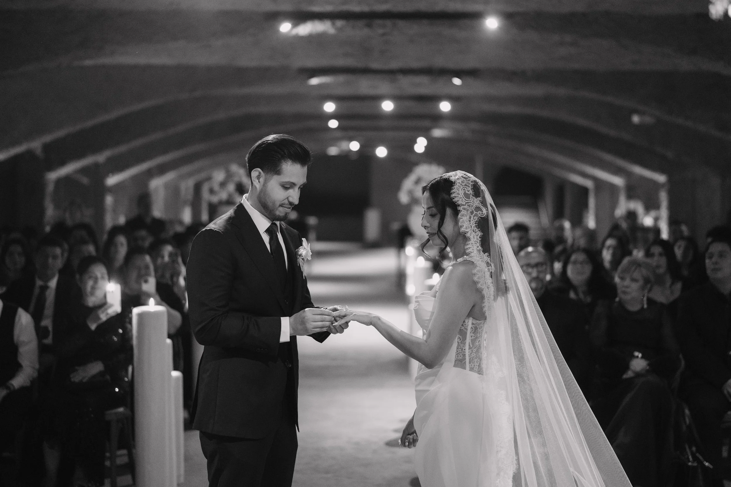 A wedding ceremony in a church with a bride and groom exchanging rings, surrounded by seated guests. Wedding Photography in Valle de Guadalupe, Ensenada, Baja California.