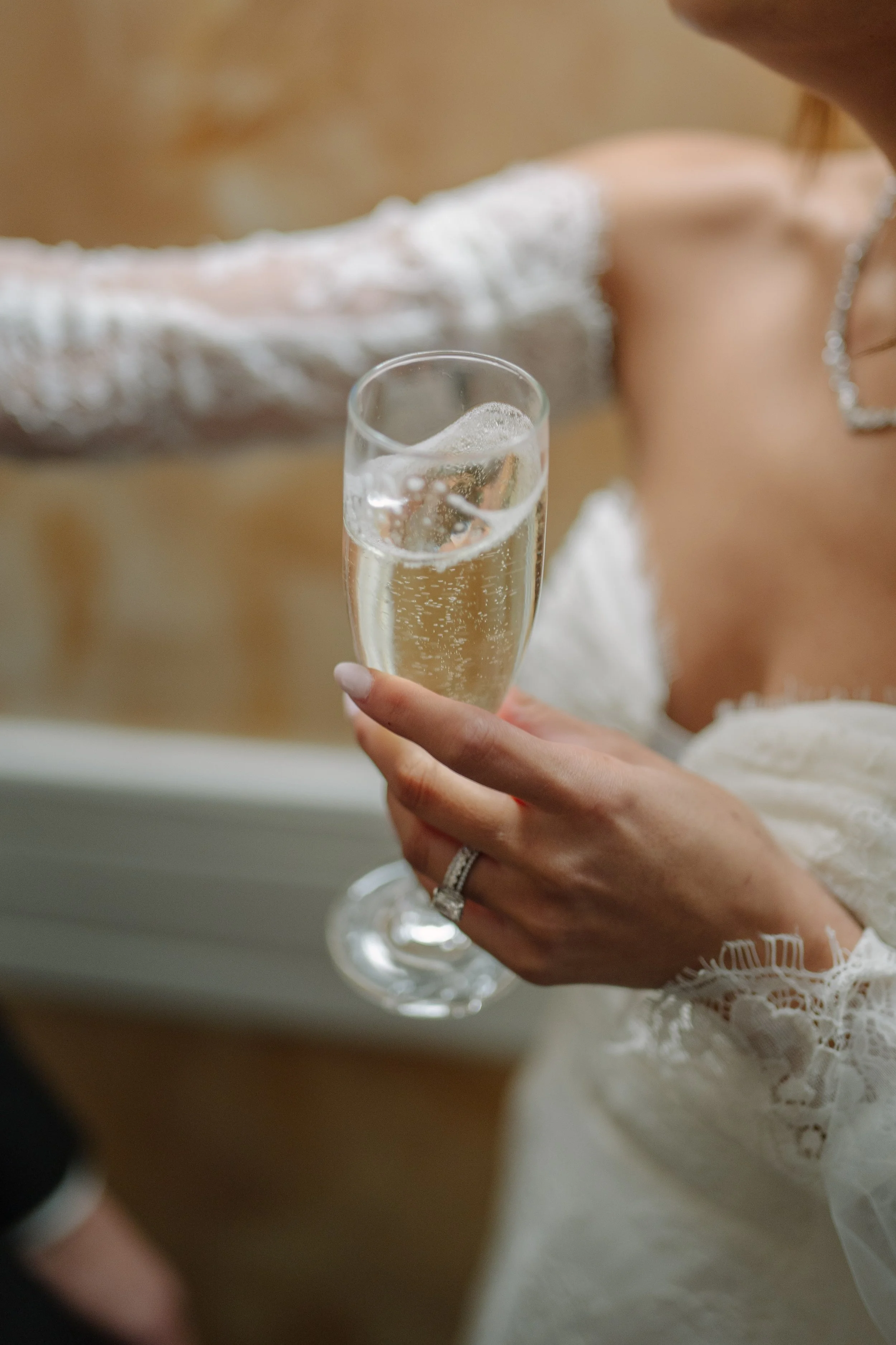 A woman in a white lace dress holding a flute of champagne. Wedding Photography in Valle de Guadalupe, Ensenada, Baja California.