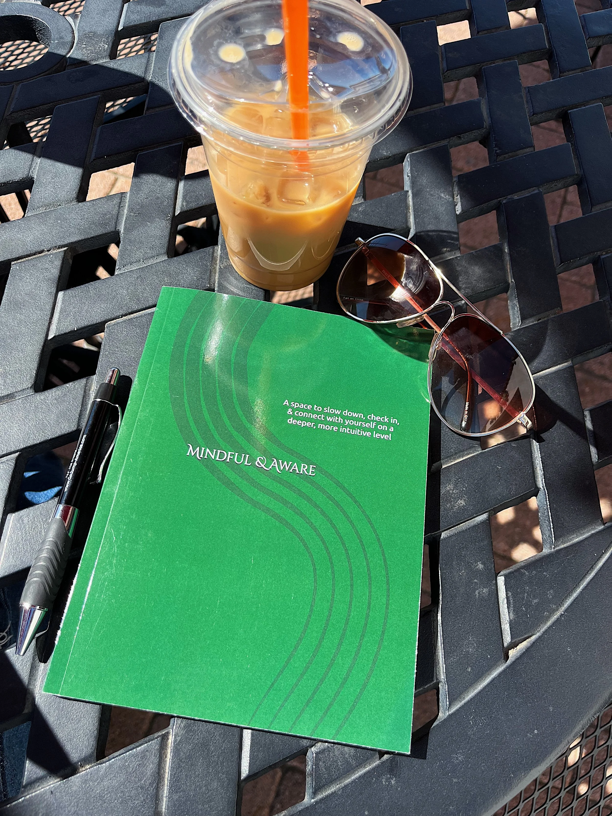 green self-care journal workbook outside on a table with a coffee and pen