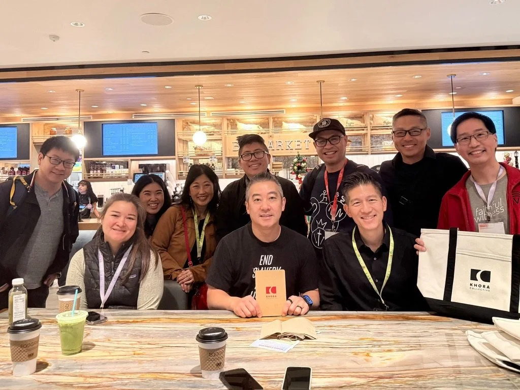 Group of nine people sitting and standing at a table in a coffee shop or cafe, smiling at the camera.