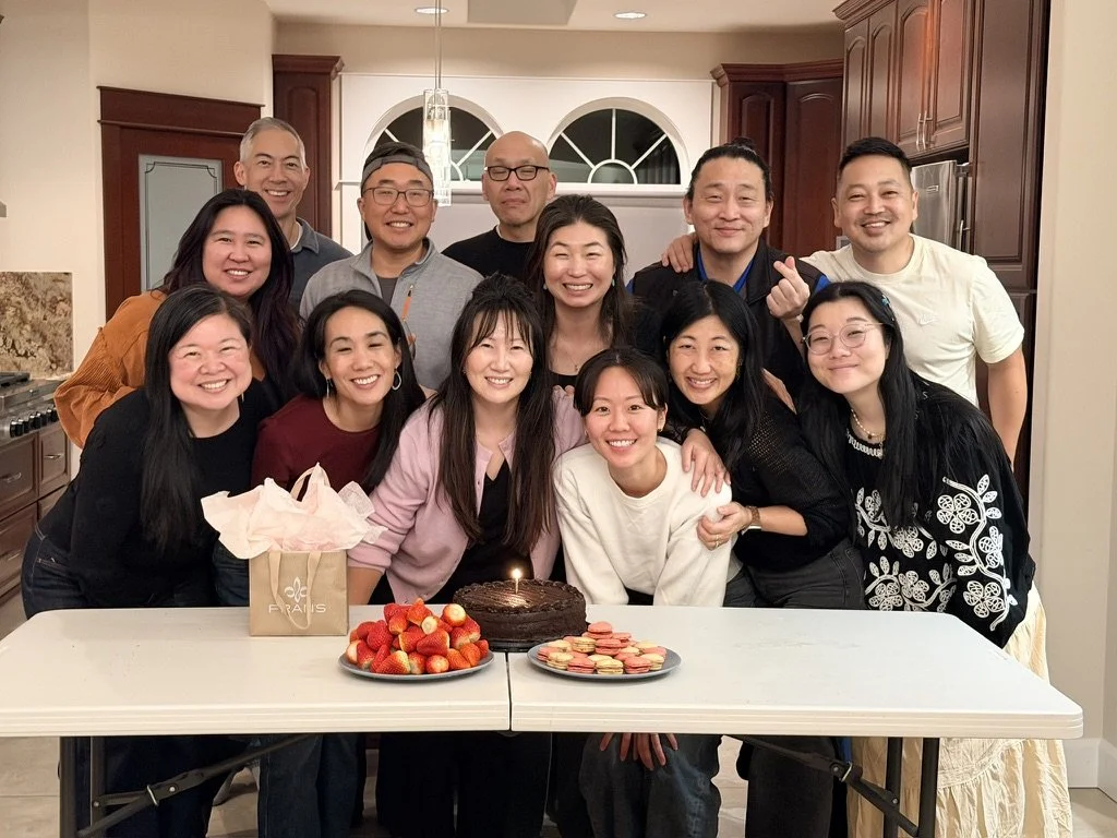 Group of people celebrating a birthday with cake and macarons in a kitchen.