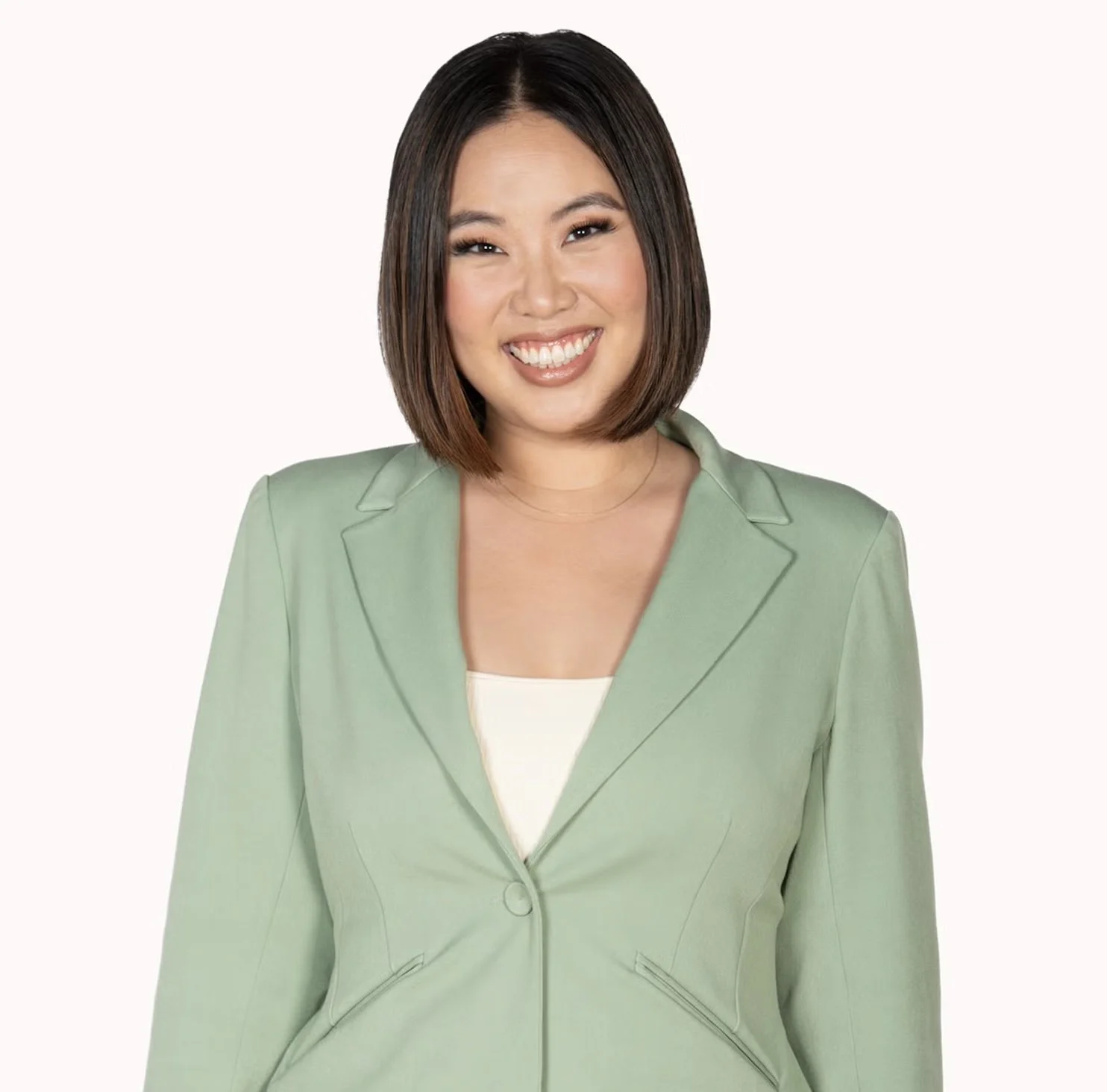 Portrait of a woman with shoulder-length brown hair wearing a light green blazer and a white top, smiling against a plain white background.