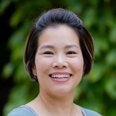 Portrait of a smiling woman outdoors with green foliage in the background.
