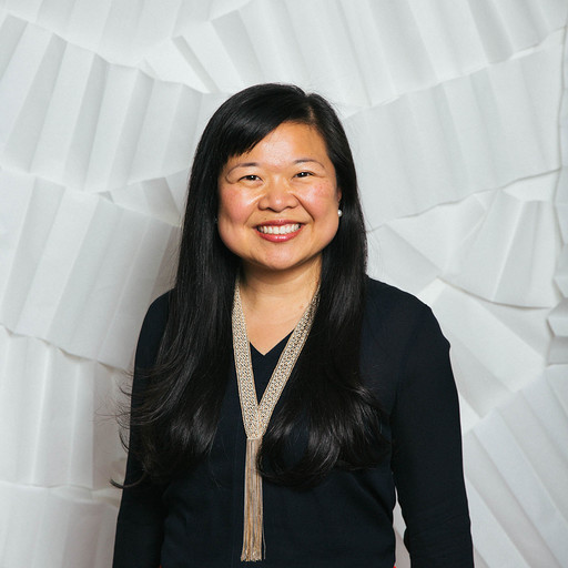 A woman with long black hair smiling in front of a white textured background.