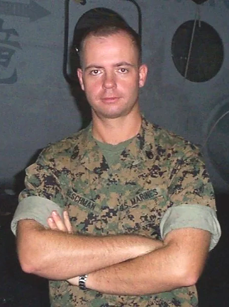 A military tank in a grassy field with trees and cloudy sky in the background, with a soldier on top.