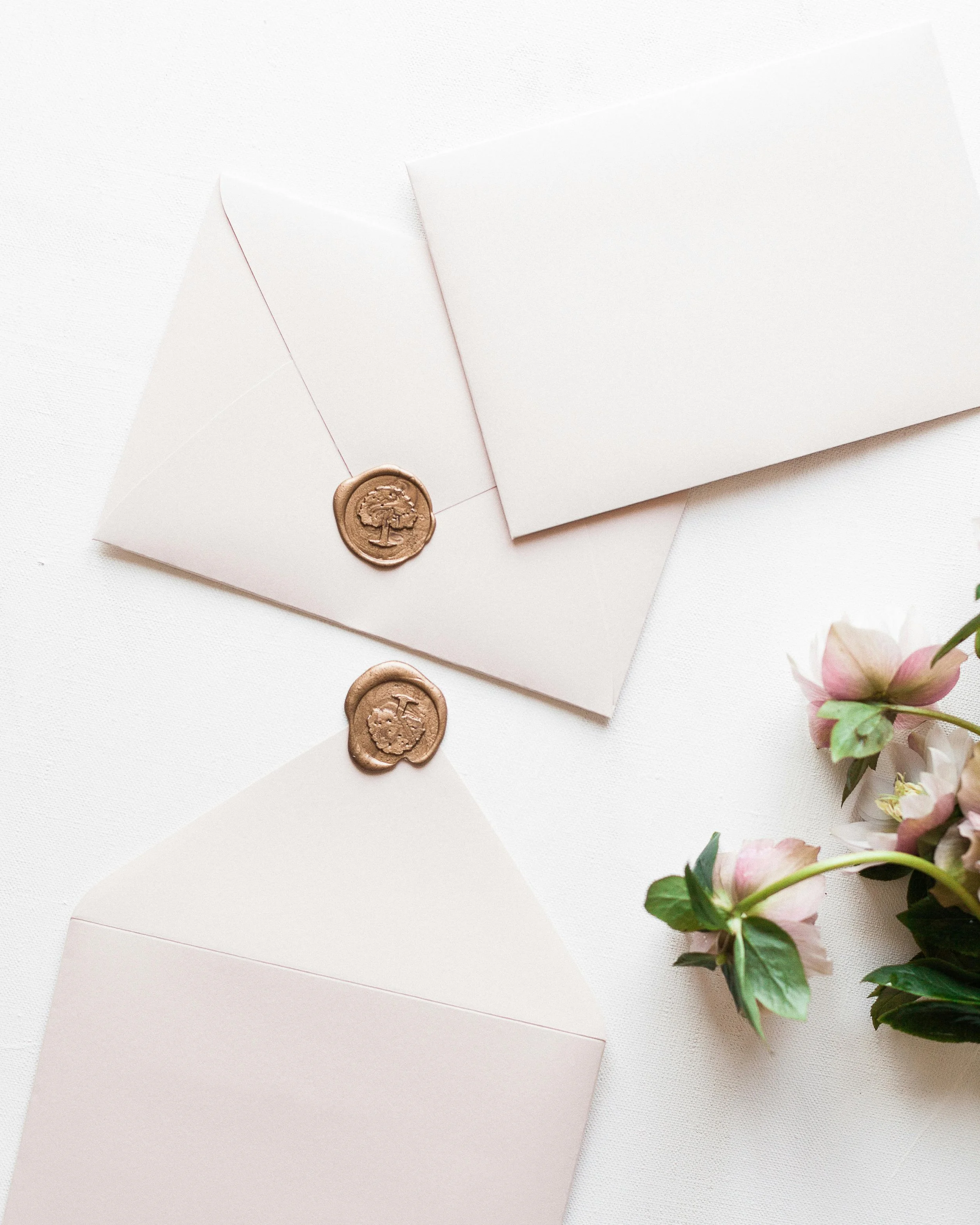 White envelopes with wax seals, arranged on a white surface, accompanied by a small bouquet of pink and white flowers.