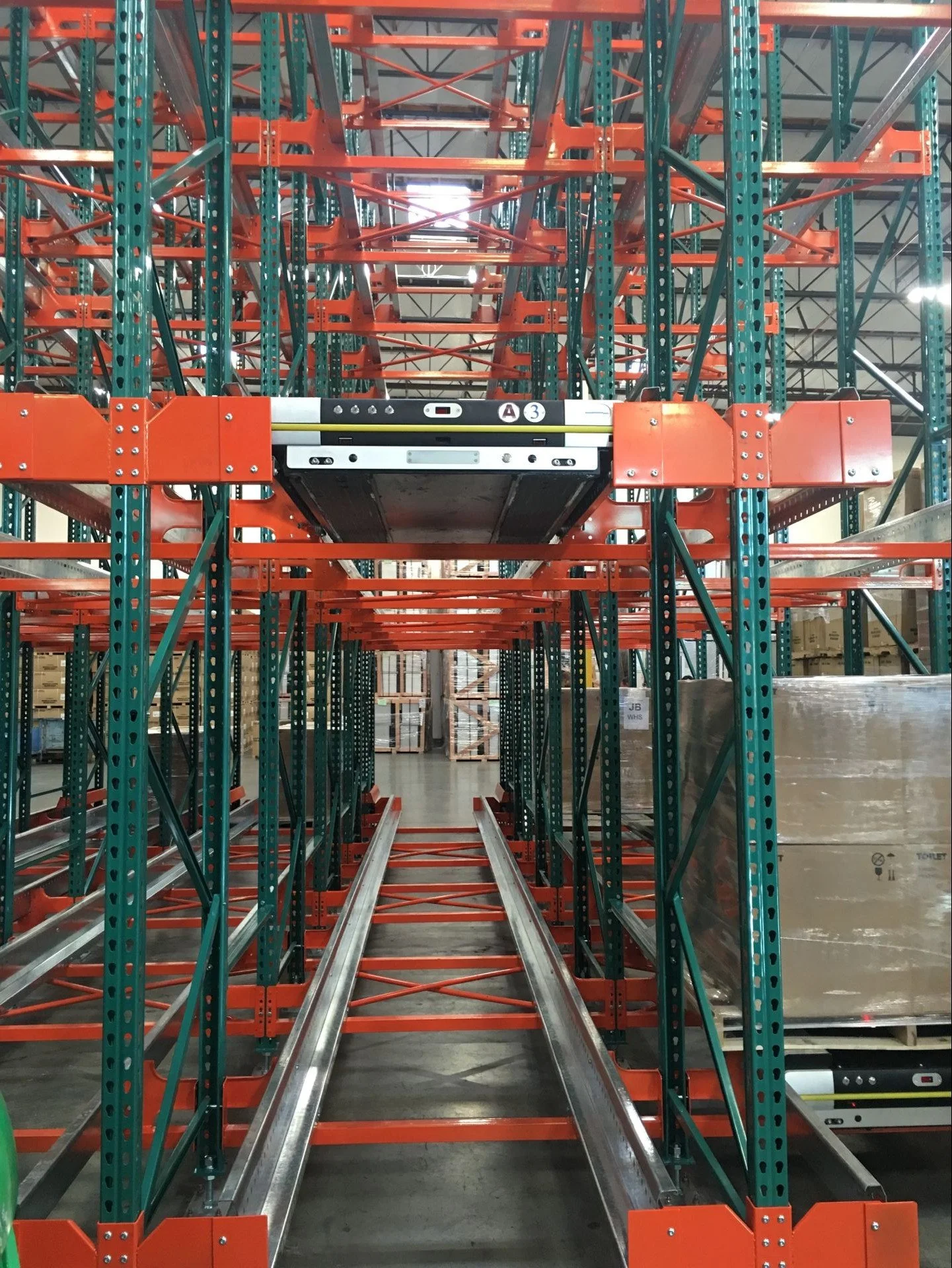 Empty warehouse with green and orange metal pallet racks and conveyor tracks.