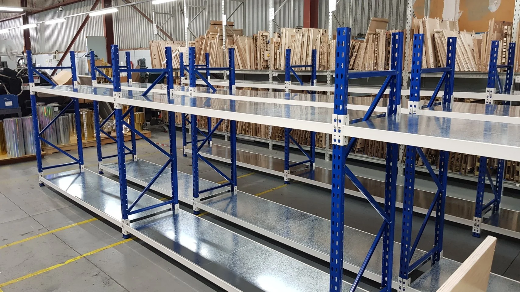 Empty warehouse shelves with blue and white metal frames, wooden boards and metal shelves in the background.