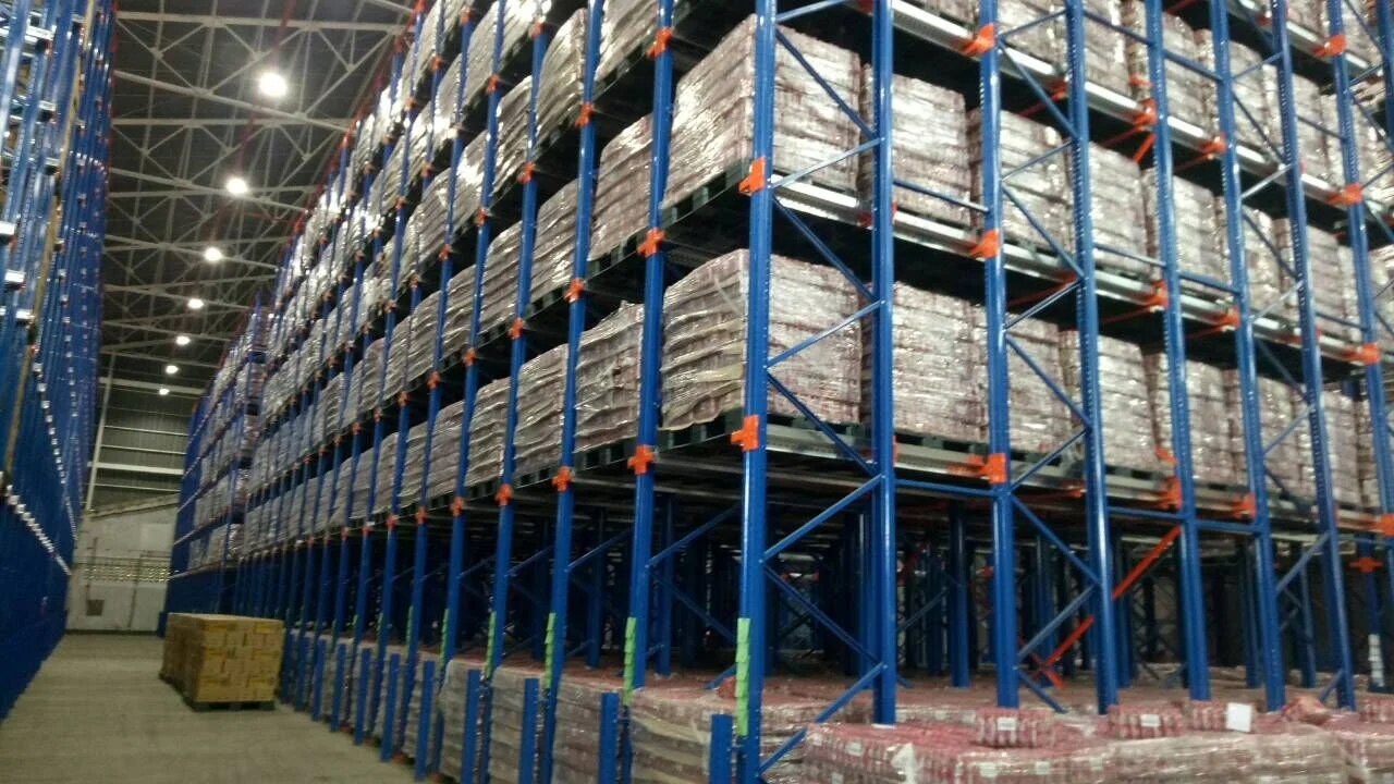 Industrial warehouse with tall blue and orange pallet racks filled with wrapped pallets of goods.
