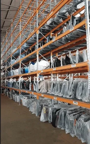 Rows of packaged computers and monitors stored on industrial shelving in a warehouse.