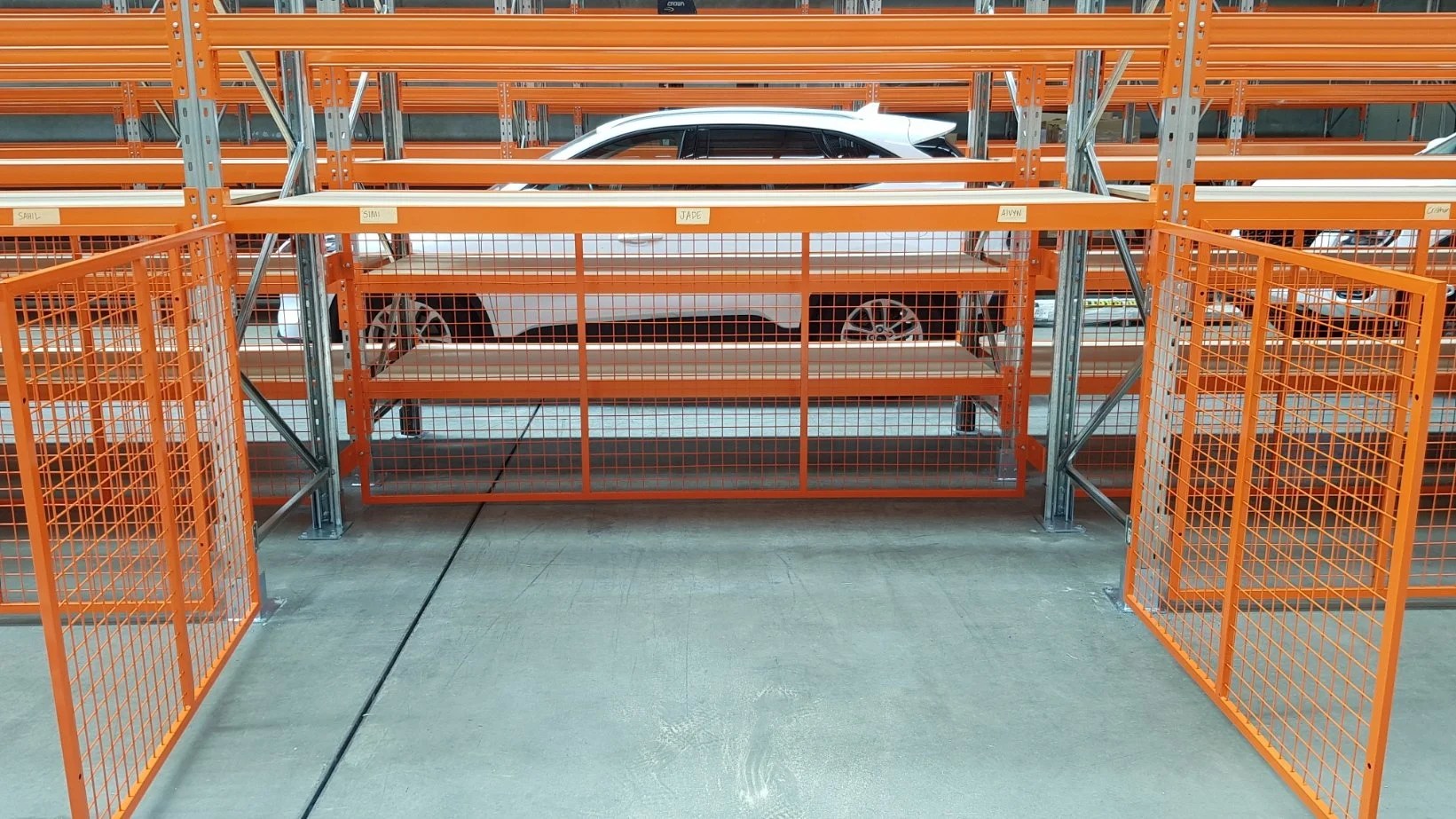 A white SUV parked in an orange metal storage rack in a warehouse or parking garage.