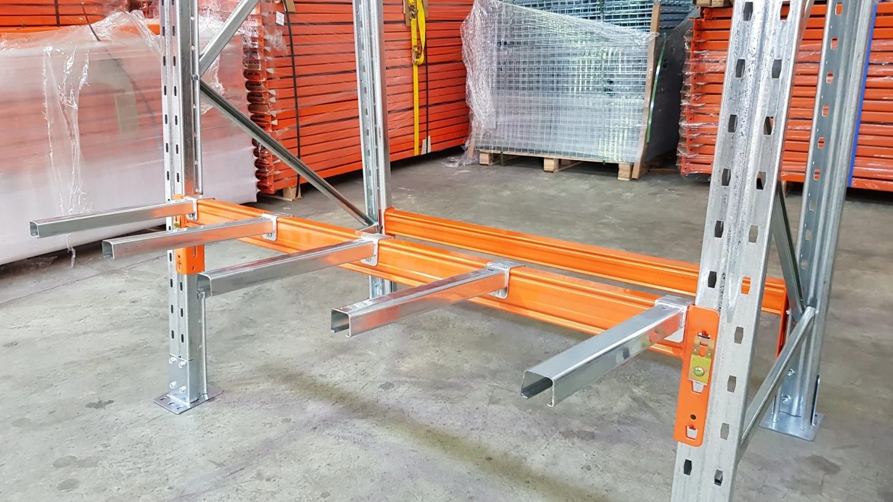 Empty steel warehouse shelving unit with orange and silver parts in a warehouse.