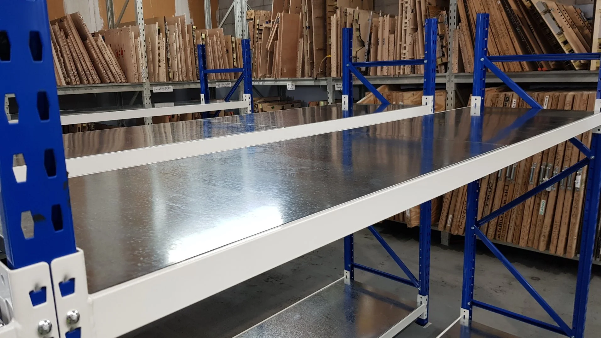 Empty industrial metal shelving unit in a hardware store, with organized wood boards and planks on shelves behind.
