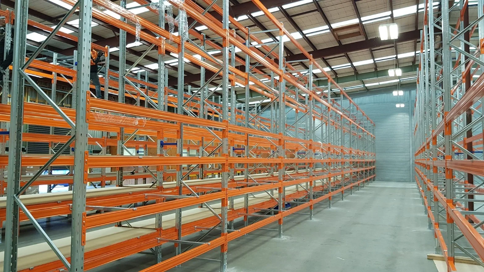 Empty warehouse shelves with orange and silver metal racks and a worker adjusting the shelves.