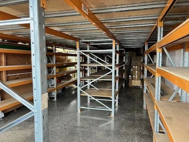 Empty industrial storage shelves with cardboard boxes and wooden pallets in a warehouse.