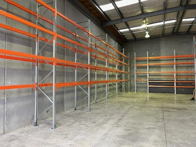 Interior of an empty warehouse with metal orange and white shelving units along the wall