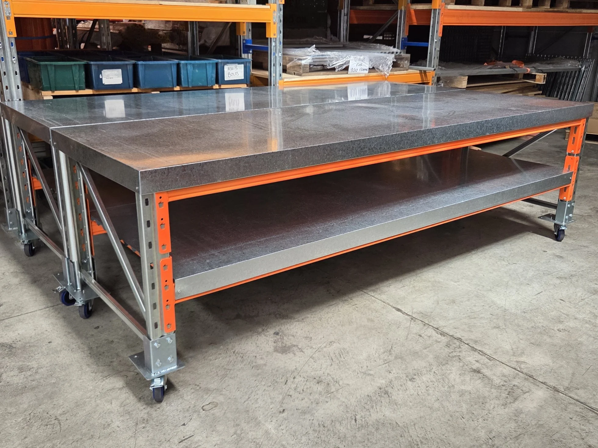 Industrial worktable with a granite top and metal shelves underneath, located in a warehouse or workshop with shelves and storage bins in the background.